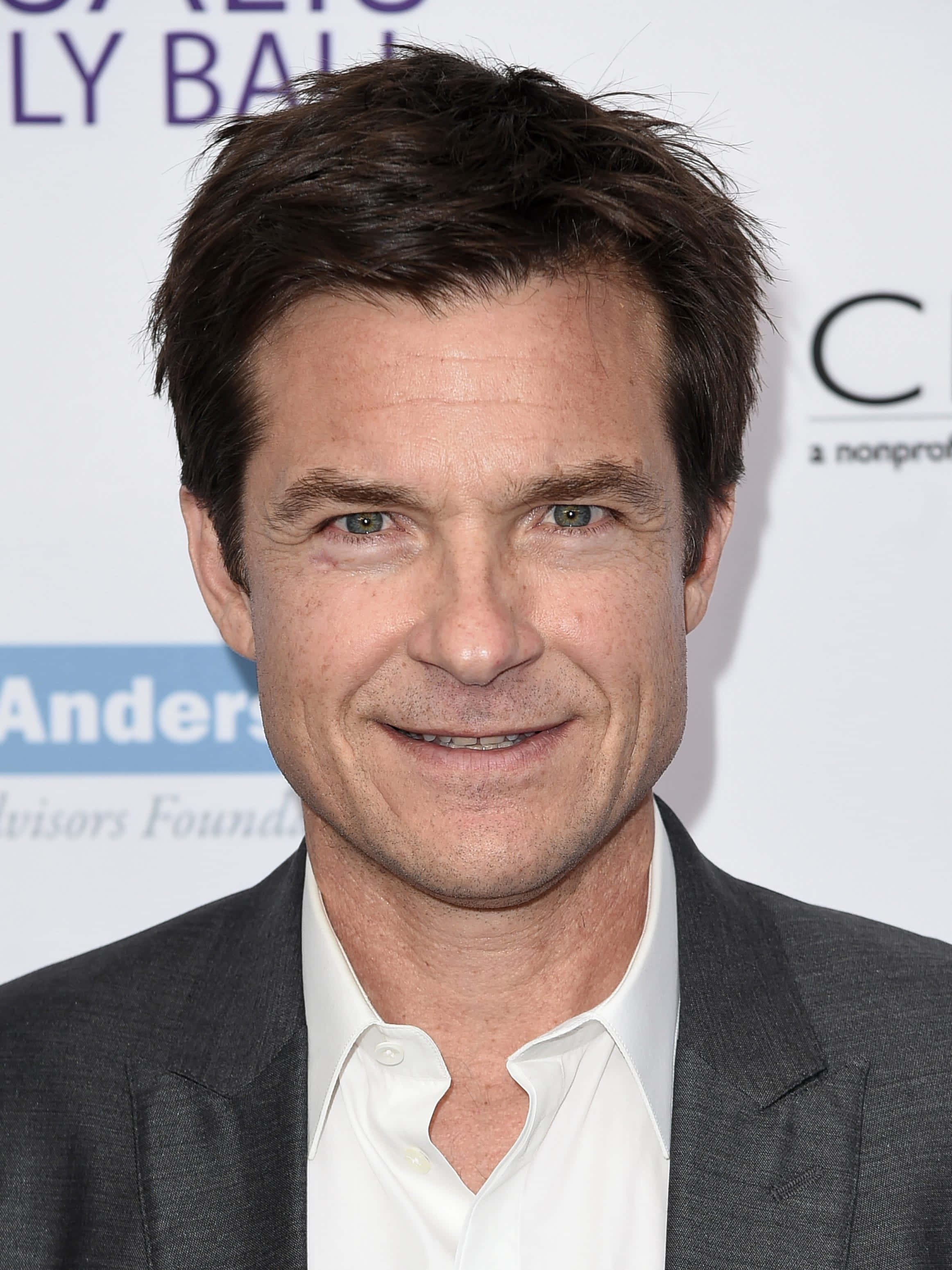 Jason Bateman 桌布 壁紙 — 一個活動中，一位黑髮微笑男士穿著灰色西裝和白色襯衫的 close-up 肖像。