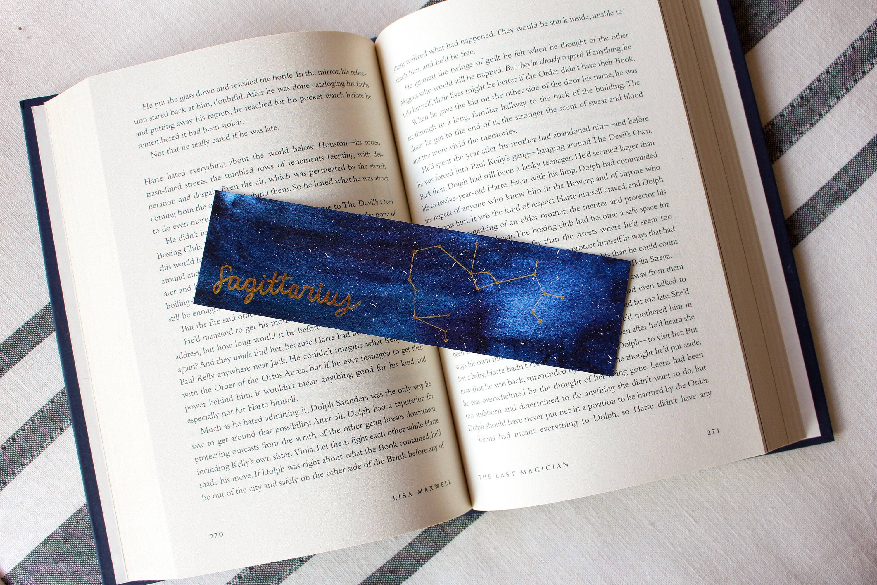 sagittarius 桌布 壁紙 — 一個海軍藍色的射手座星座書籤放在一本打開的書上，書上有印刷文字和頁碼。