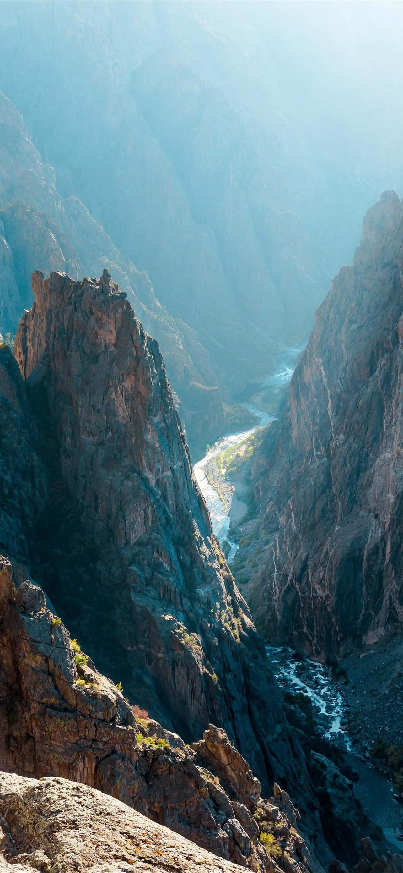 Black Canyon 桌布 壁紙 — 一個深峽谷的壯麗景色，陡峭的岩石懸崖和下方蜿蜒的河流沐浴在明亮的陽光中。