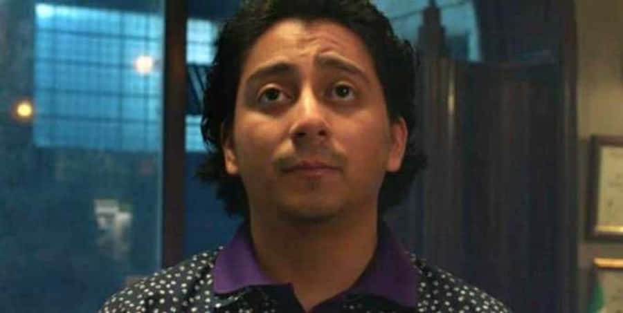 Flash Thompson 桌布 壁紙 — 一個深色捲髮、身穿波點襯衫的男人，在昏暗的房間裡向上看，露出驚訝的表情。