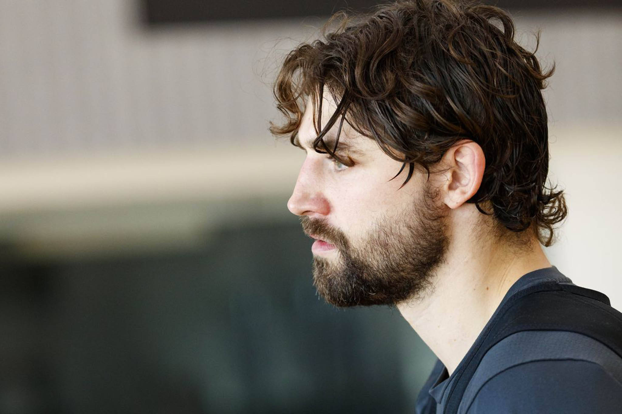 joe harris 桌布 壁紙 — 一個深色捲髮留鬍子的男人在柔和模糊的室內環境中若有所思地望向一邊。