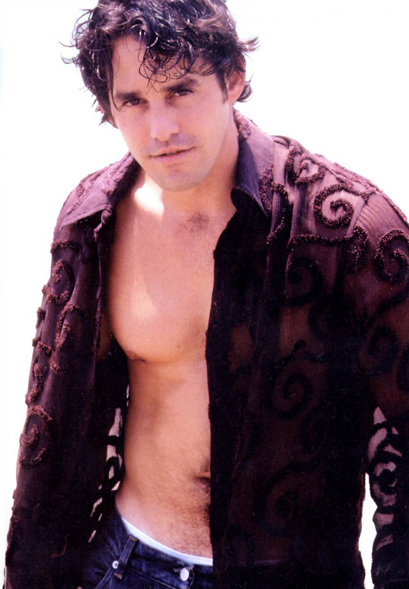 Nicholas Brendon 桌布 壁紙 — 一個深色捲髮的男人穿著一件敞開的華麗深色襯衫，在明亮的白色背景下露出他的胸膛。