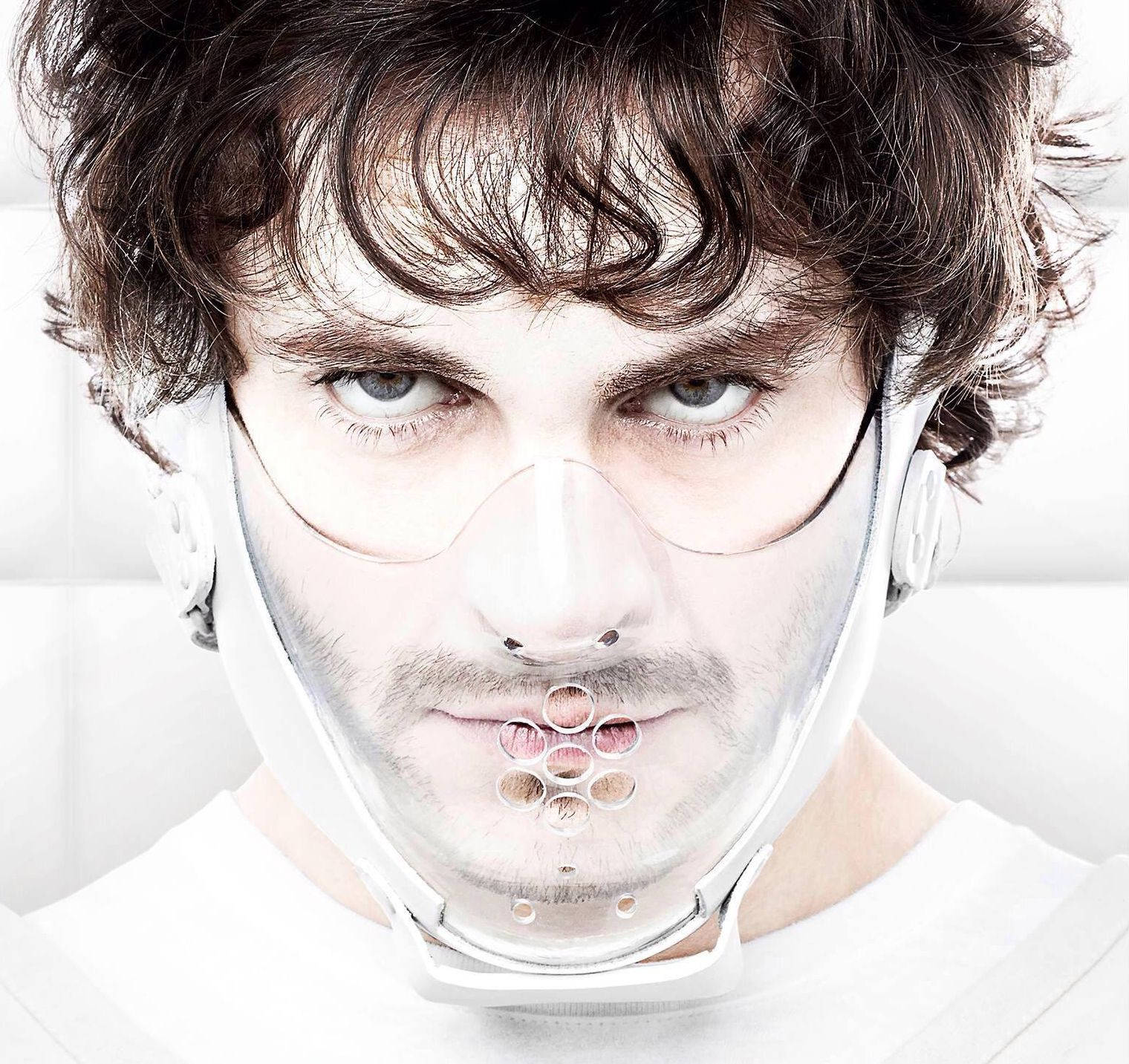 Hugh Dancy 桌布 壁紙 — 一個深色捲髮的男人透過一個在嘴巴位置有圓形鏤空的透明塑膠面罩凝視著。