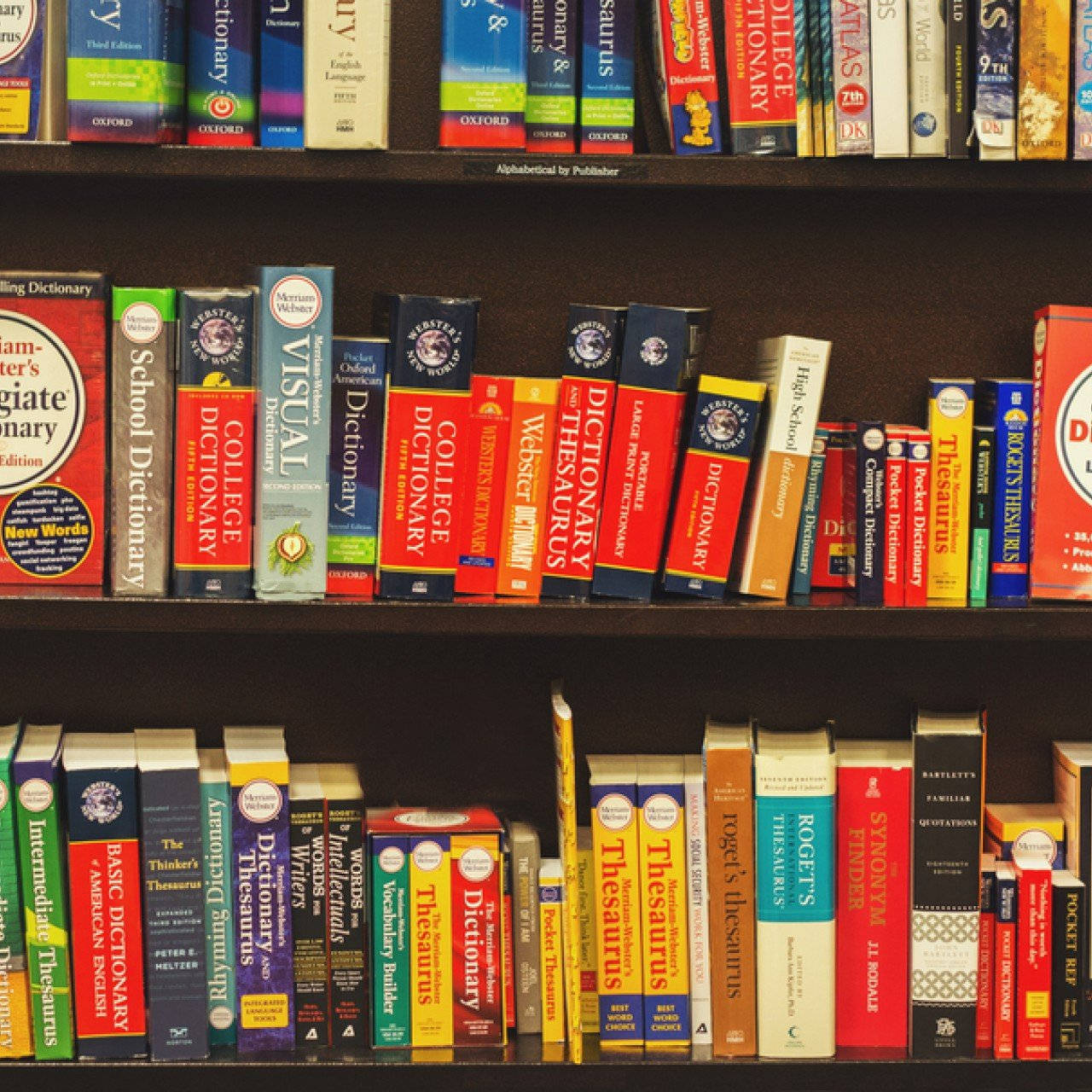 Dictionary 桌布 壁紙 — 一個深色木書架的近距離特寫，裡面裝滿了色彩繽紛的參考書，如字典和同義詞詞典。