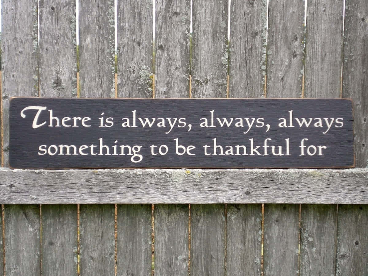 Thankful 桌布 壁紙 — 一個深色木牌，上面有白色草書文字寫著「There is always, always, always something to be thankful for」，安裝在一個風化的灰色木柵欄上。