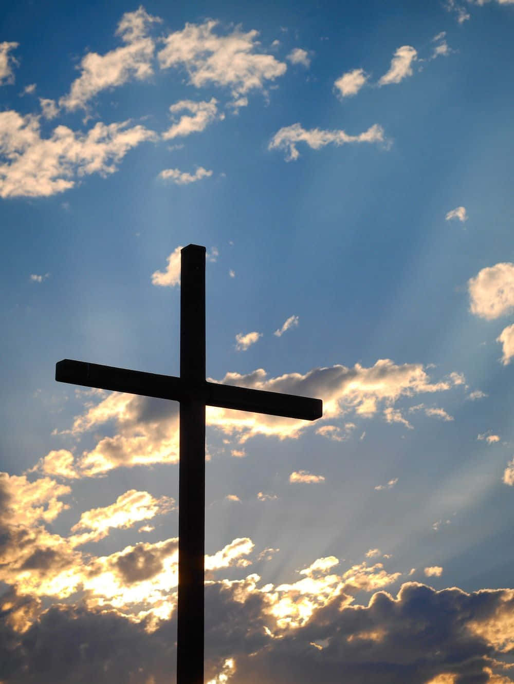 Beautiful Cross 桌布 壁紙 — 一個深色木製十字架在充滿活力的藍天背景下呈現剪影，金色陽光穿透散落的雲層。