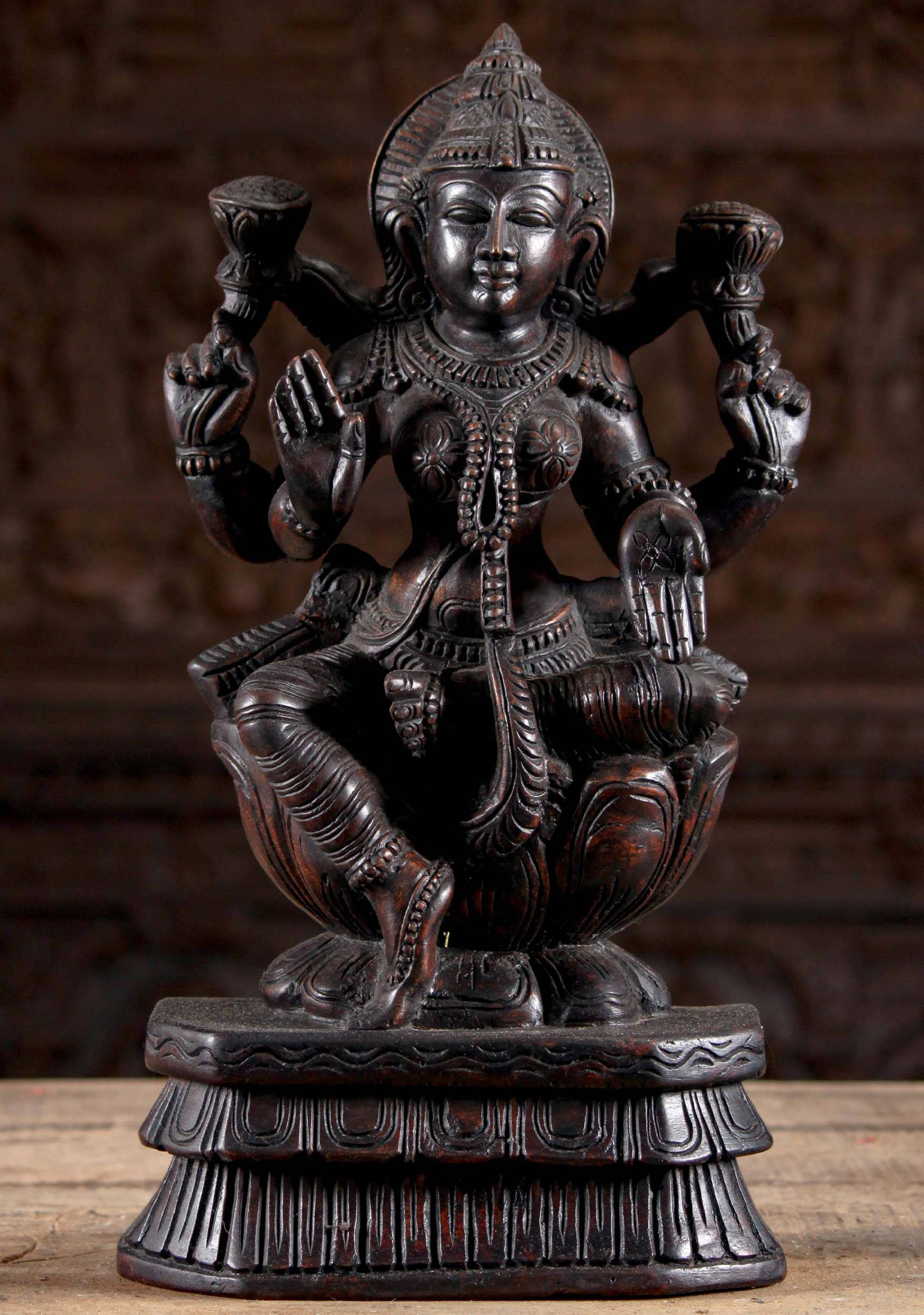 Lakshmi Devi 桌布 壁紙 — 一個深色木製的多臂印度教神像，以蓮花坐姿坐在一個裝飾華麗、雕刻精細的底座上。
