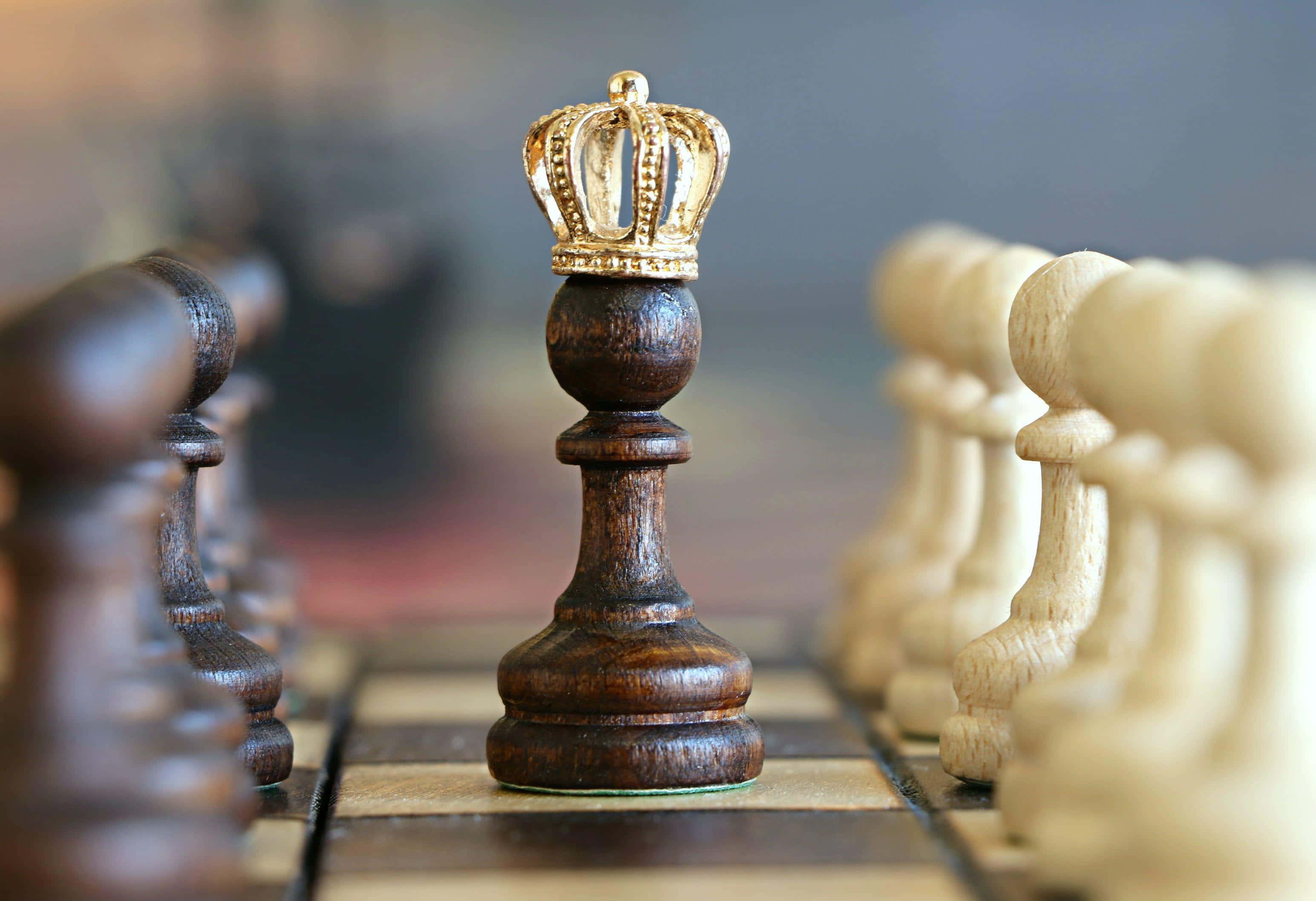 西洋棋 桌布 壁紙 — 一個深色木製西洋棋國王戴上金色王冠的特寫，立於棋盤上，背景有模糊的對手棋子。