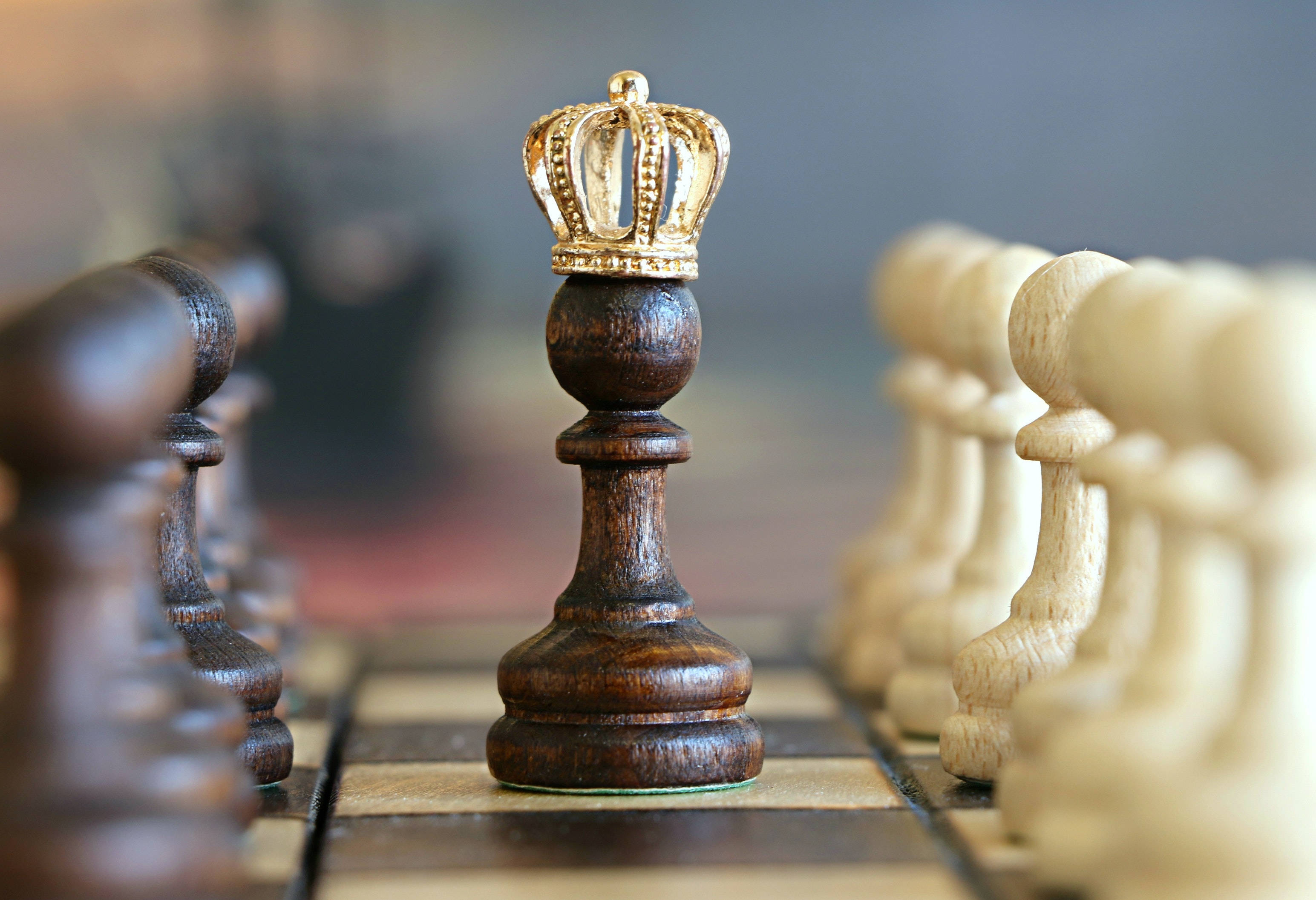King And Queen 桌布 壁紙 — 一個深色木製西洋棋國王戴著金色王冠，站在棋盤上，面對白色棋子的特寫。