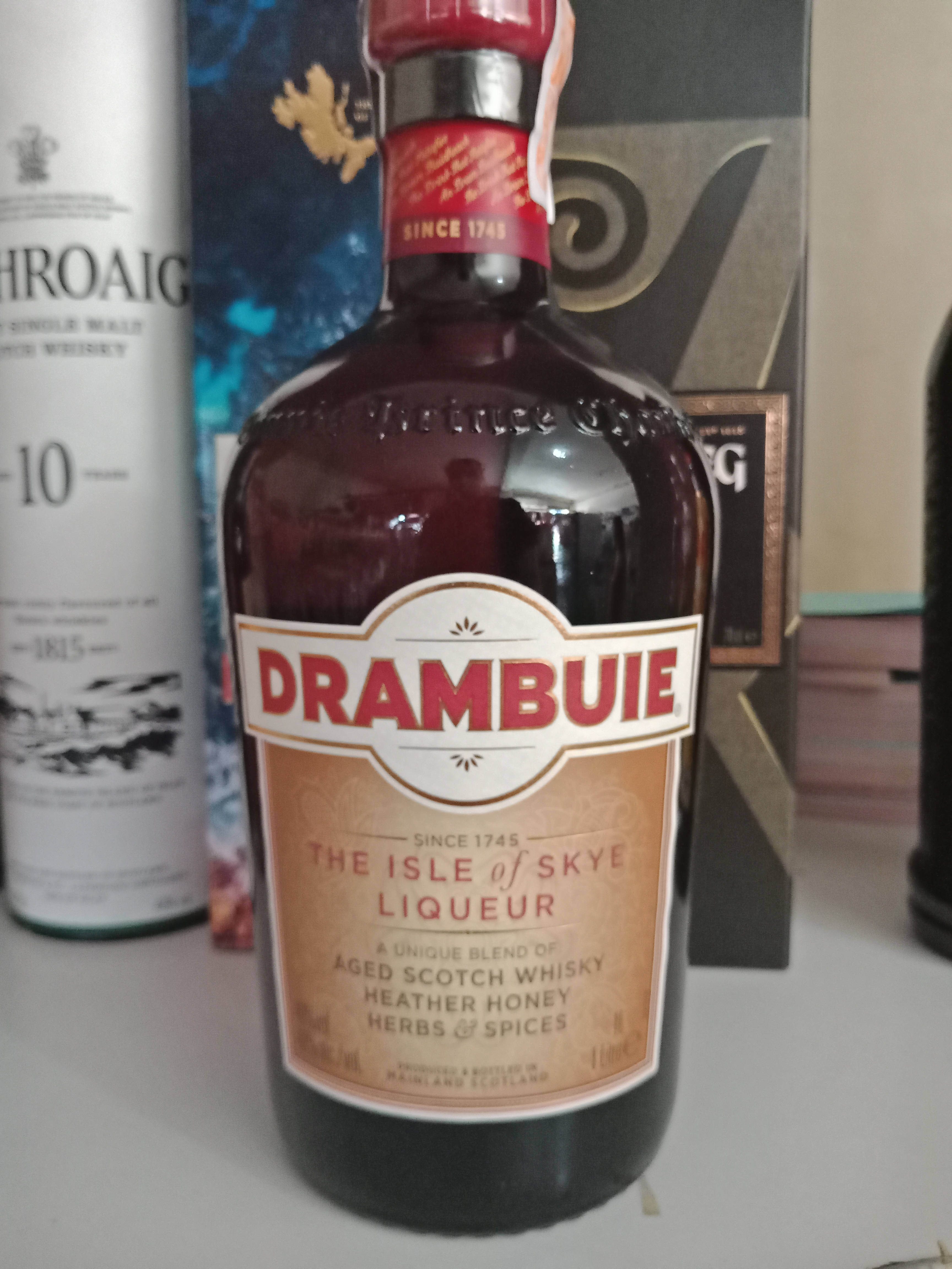 alcohol 桌布 壁紙 — 一個深色玻璃瓶的 Drambuie 利口酒特寫，帶有紅色瓶蓋和米色標籤，旁邊是架子上的其他威士忌酒瓶。