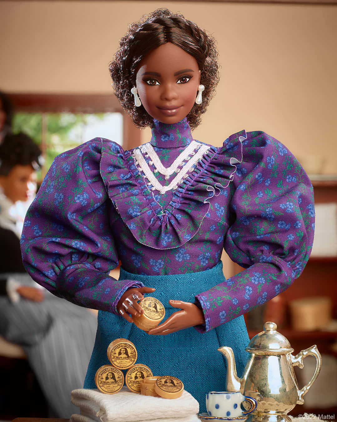 Barbie Doll 桌布 壁紙 — 一個深色皮膚、捲曲頭髮的玩偶，穿著紫色花卉襯衫和藍色圍裙，拿著一罐蜂蜜，桌上還有蜂蜜罐和一個銀色茶壺。