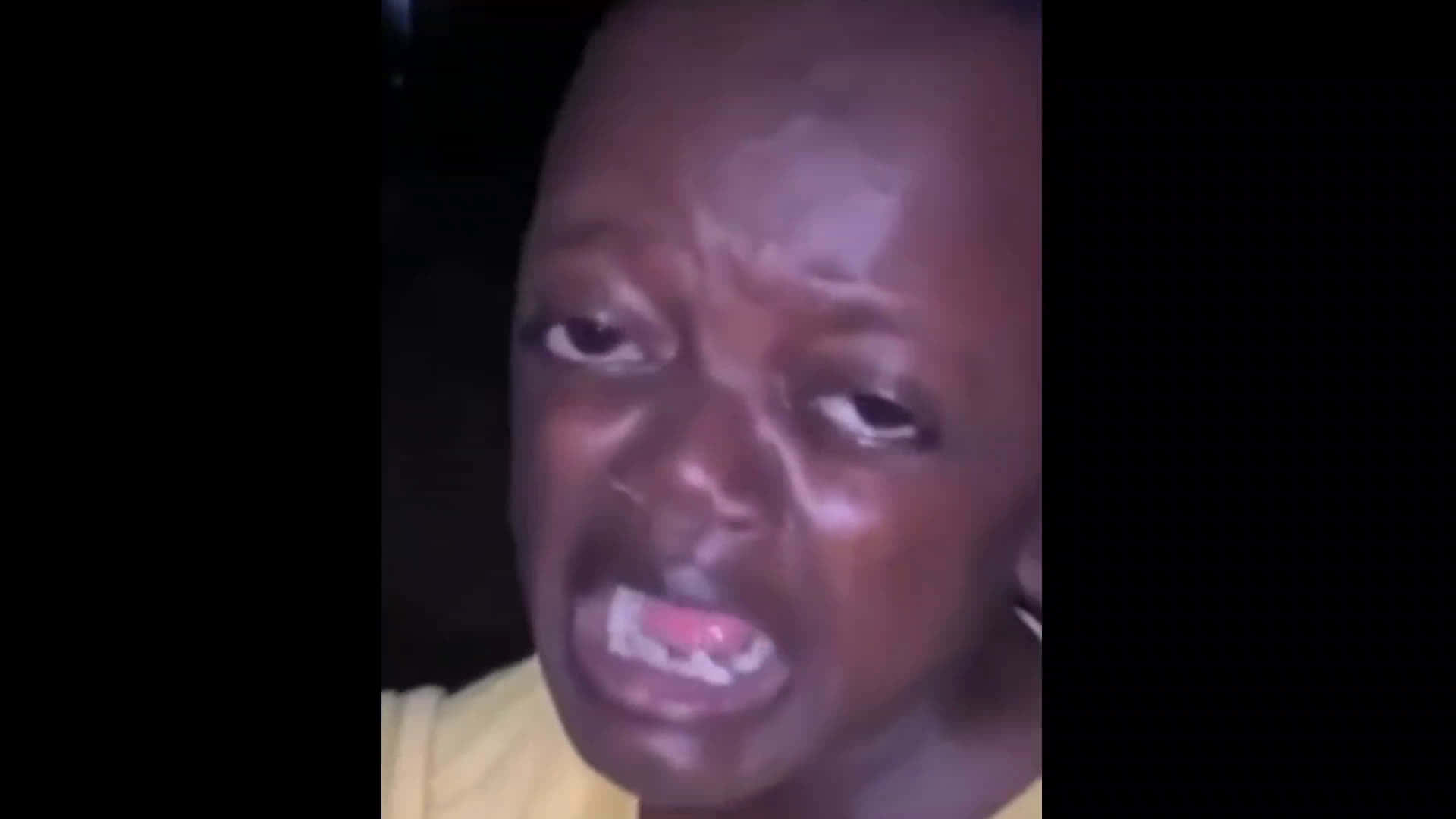 搞笑 桌布 壁紙 — 一個深色皮膚、穿著黃色襯衫的人，在昏暗的環境中張開牙齒、睜大眼睛尖叫。