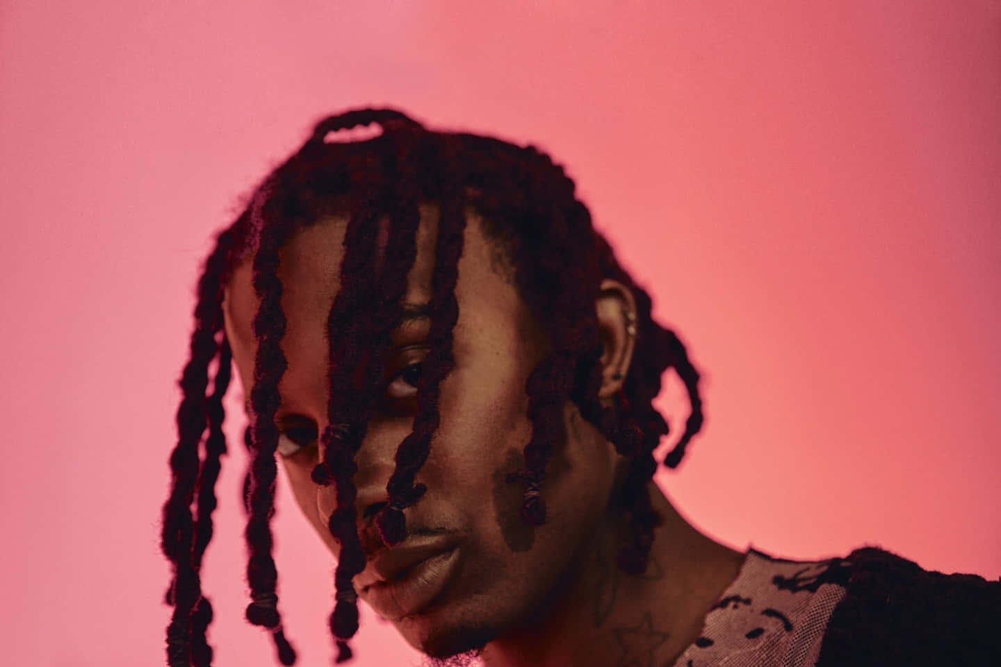 Playboi Carti 桌布 壁紙 — 一個深色辮子的人，在柔和的粉紅色工作室背景下凝視著。