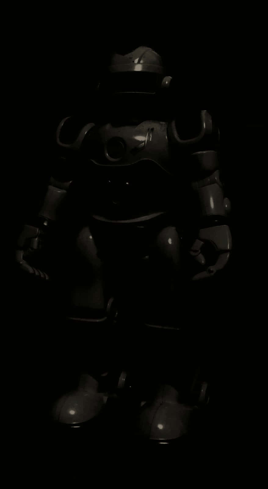Robot 3D 壁紙 — 一個深色金屬機器人在近乎全黑的環境中靜止不動，其關節和頭盔上有微弱的高光。