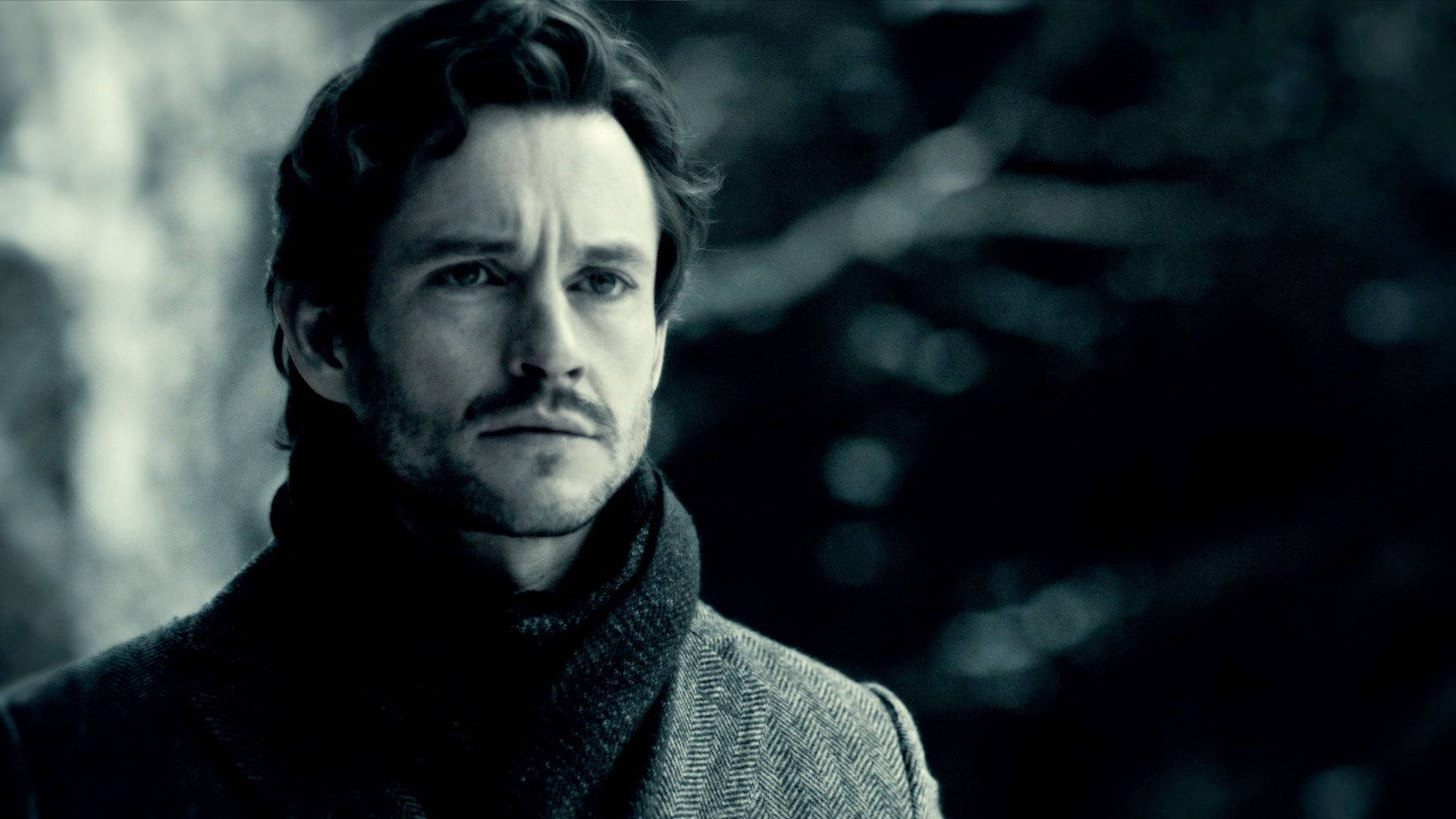 Hugh Dancy 桌布 壁紙 — 一個深色頭髮、戴著圍巾的男人，在模糊的森林背景下，以冷藍色調專注地凝視。