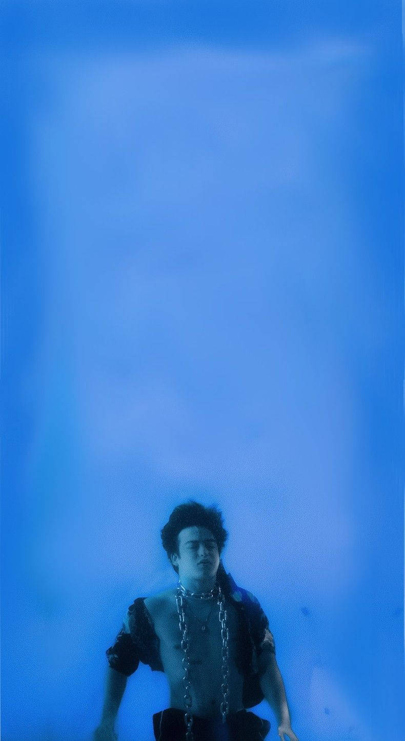 joji 桌布 壁紙 — 一個深色頭髮、戴著鎖鏈的人浸沒在朦朧的藍色水下環境中。