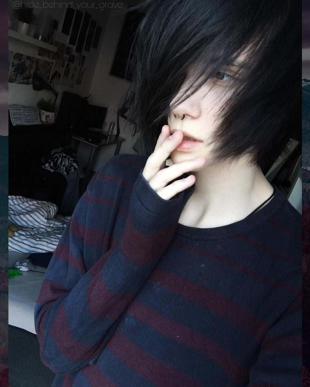 emo 美學 桌布 壁紙 — 一個深色頭髮、戴鼻環的人穿著條紋毛衣，在雜亂的房間裡將手放在嘴邊。