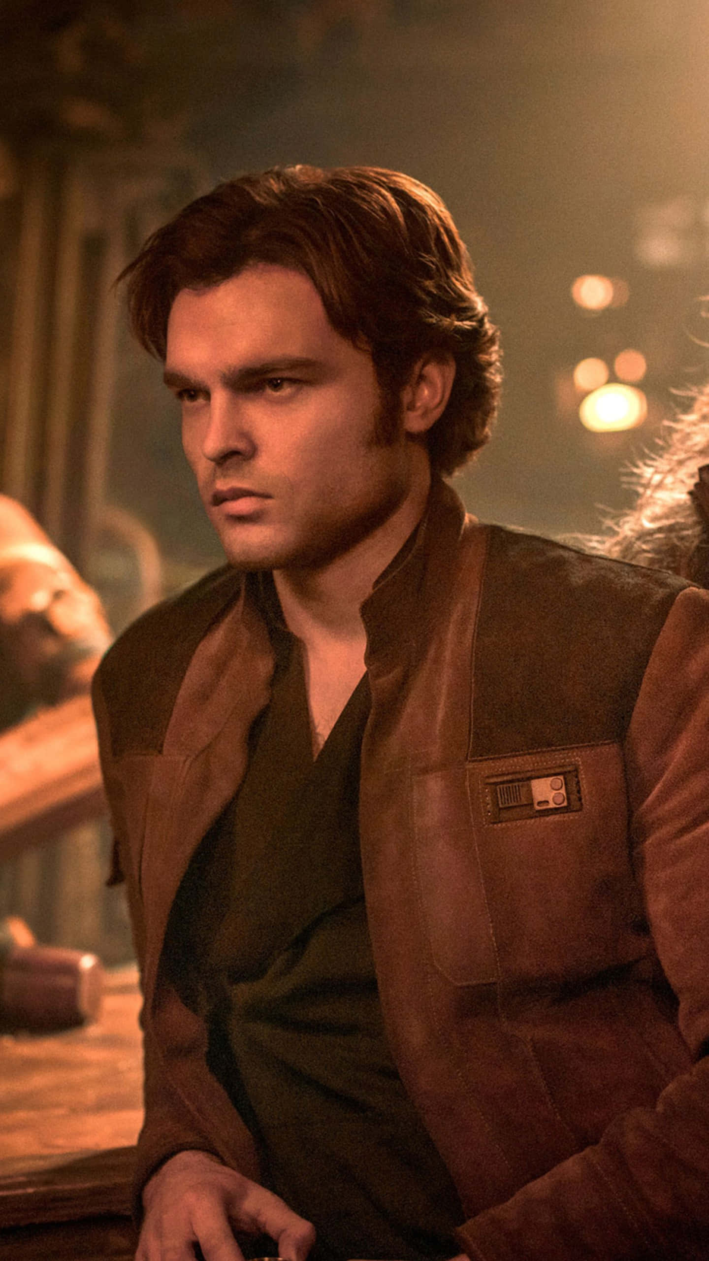 Solo A Star Wars Story 桌布 壁紙 — 一個深色頭髮、眼神銳利的男人，在燈光昏暗、溫暖的酒吧裡穿著棕色皮夾克。