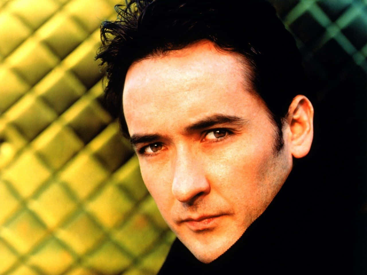 John Cusack 桌布 壁紙 — 一個深色頭髮、眼神銳利的男士特寫肖像，背景為帶有紋理的金黃色。