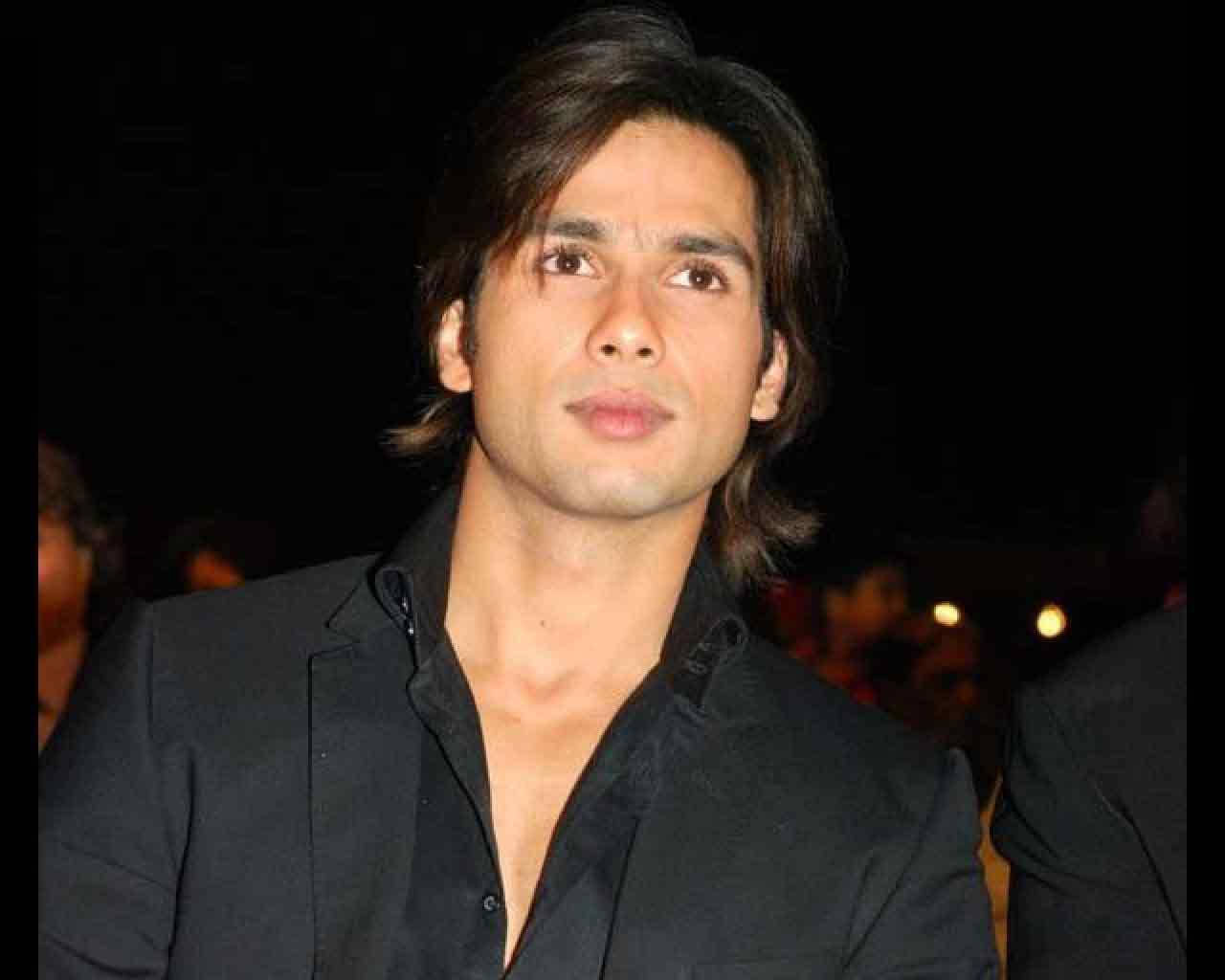 Shahid Kapoor 桌布 壁紙 — 一個深色頭髮、身穿黑色襯衫的男子，在模糊的夜間背景和柔和散景燈光下若有所思地凝視著。