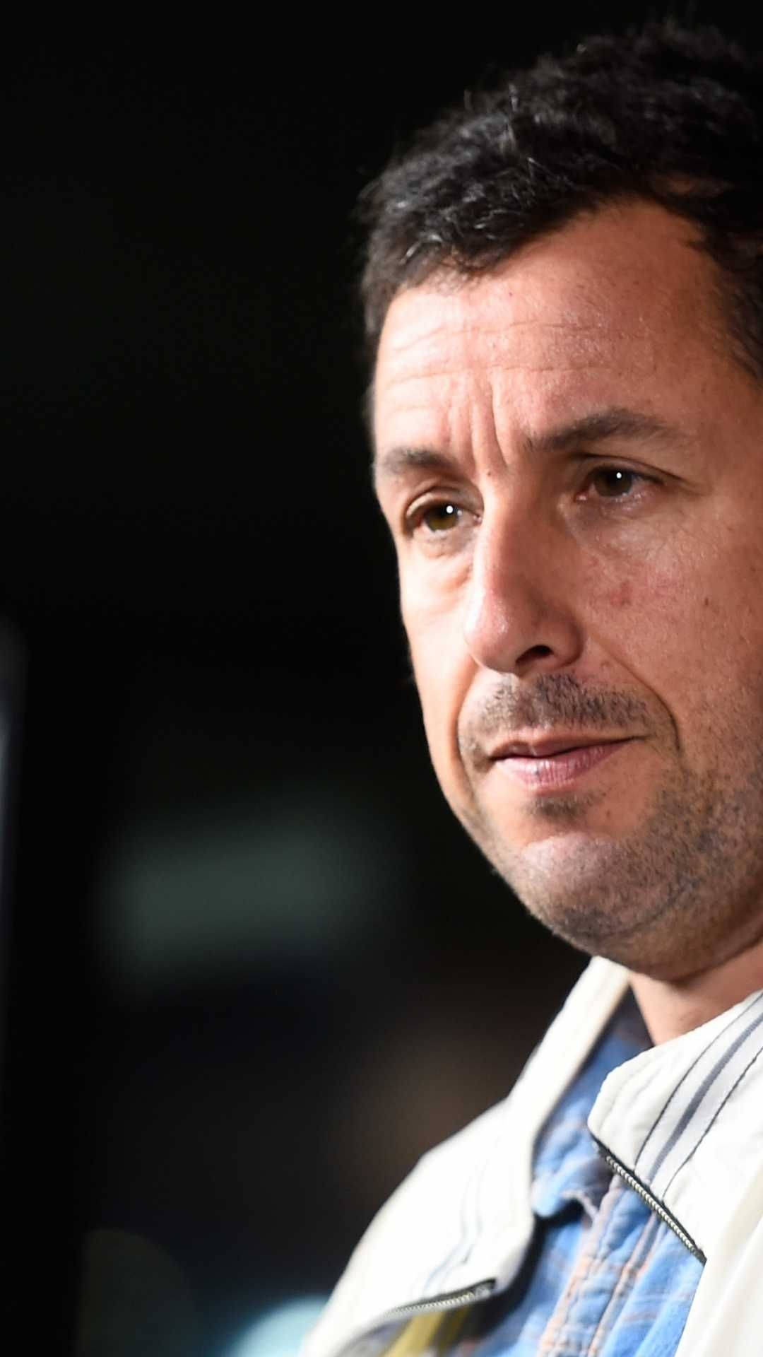 Adam Sandler 桌布 壁紙 — 一個深色頭髮、鬍渣男人的特寫肖像，他穿著白色外套和藍色襯衫，背景是暗色模糊的。