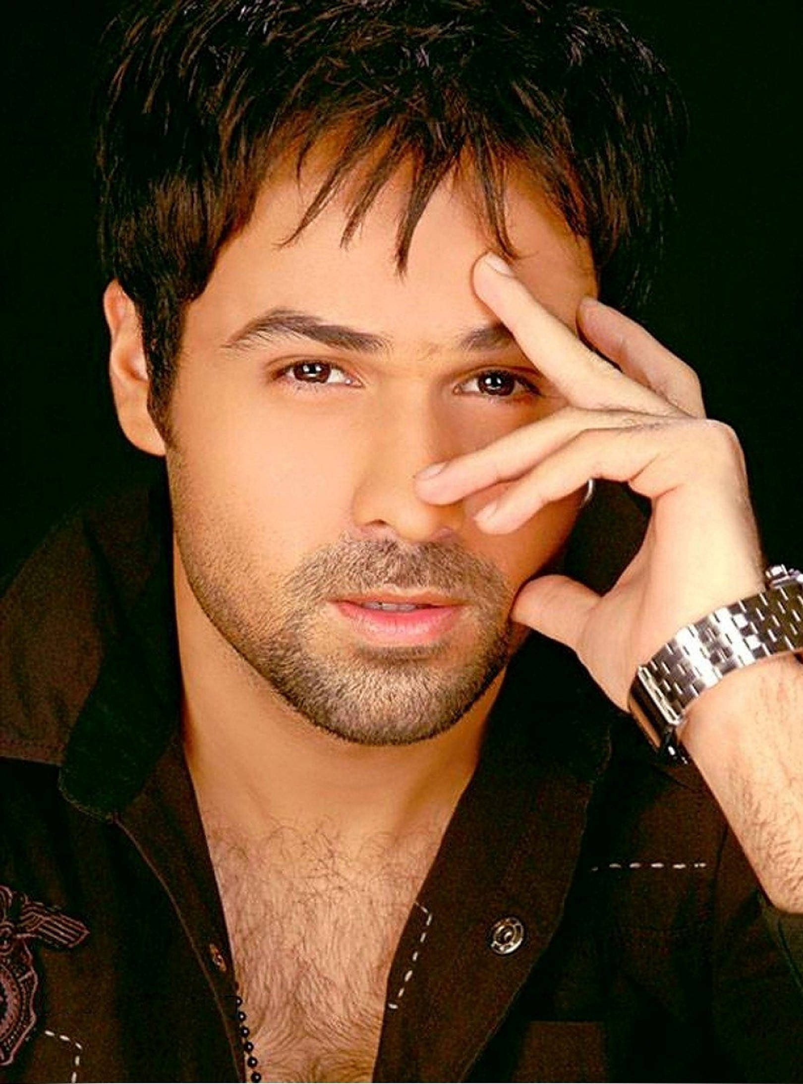 Emraan Hashmi 桌布 壁紙 — 一個深色頭髮和鬍鬚的男人，在黑色背景前將手放在臉附近，直視鏡頭。