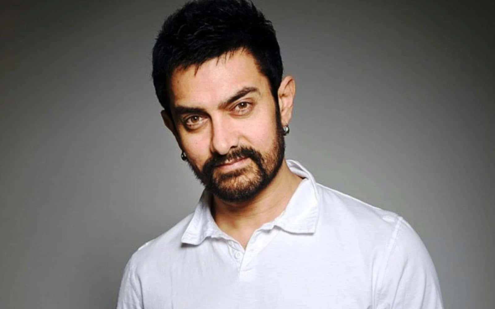 Aamir Khan 桌布 壁紙 — 一個深色頭髮和鬍鬚的男人，穿著白色Polo衫，背景是純灰色。
