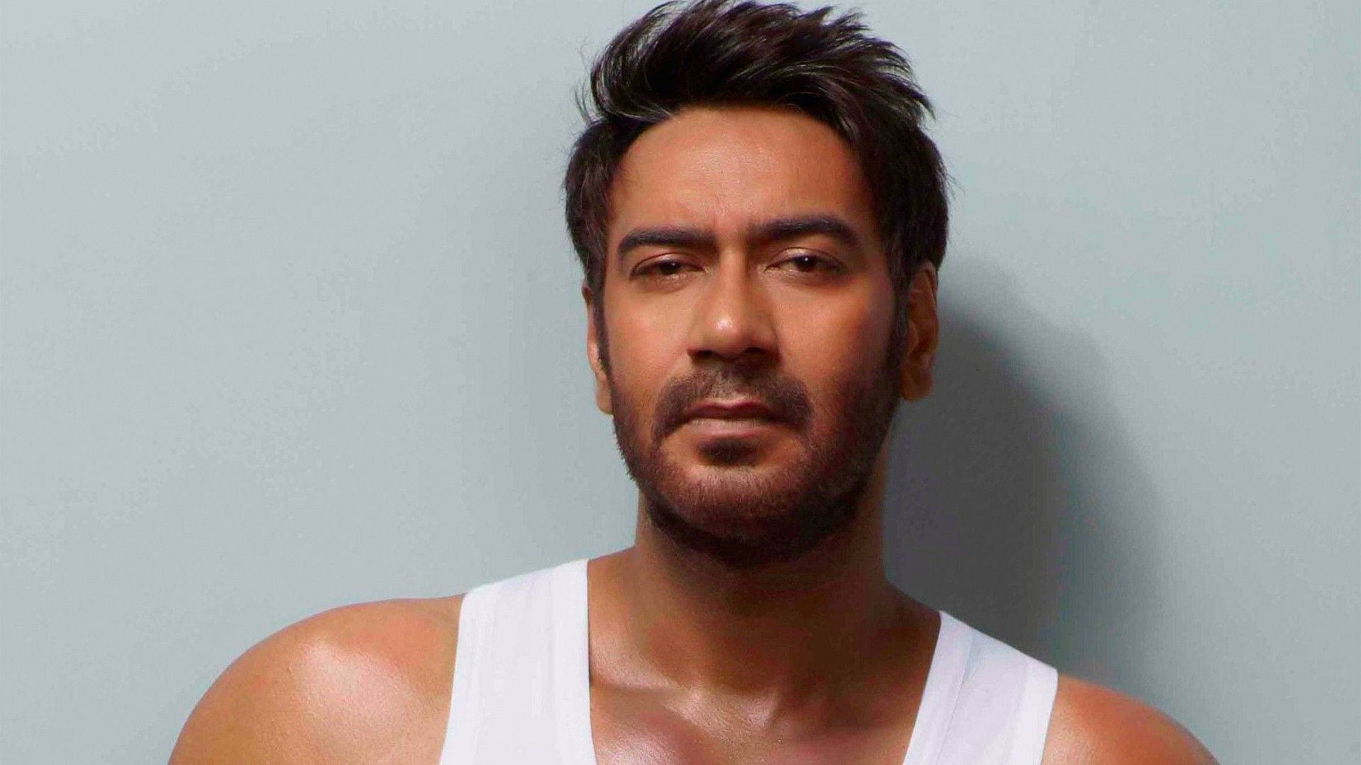 ajay devgn 桌布 壁紙 — 一個深色頭髮和鬍鬚的男人，穿著白色背心，背景是純淺灰色。
