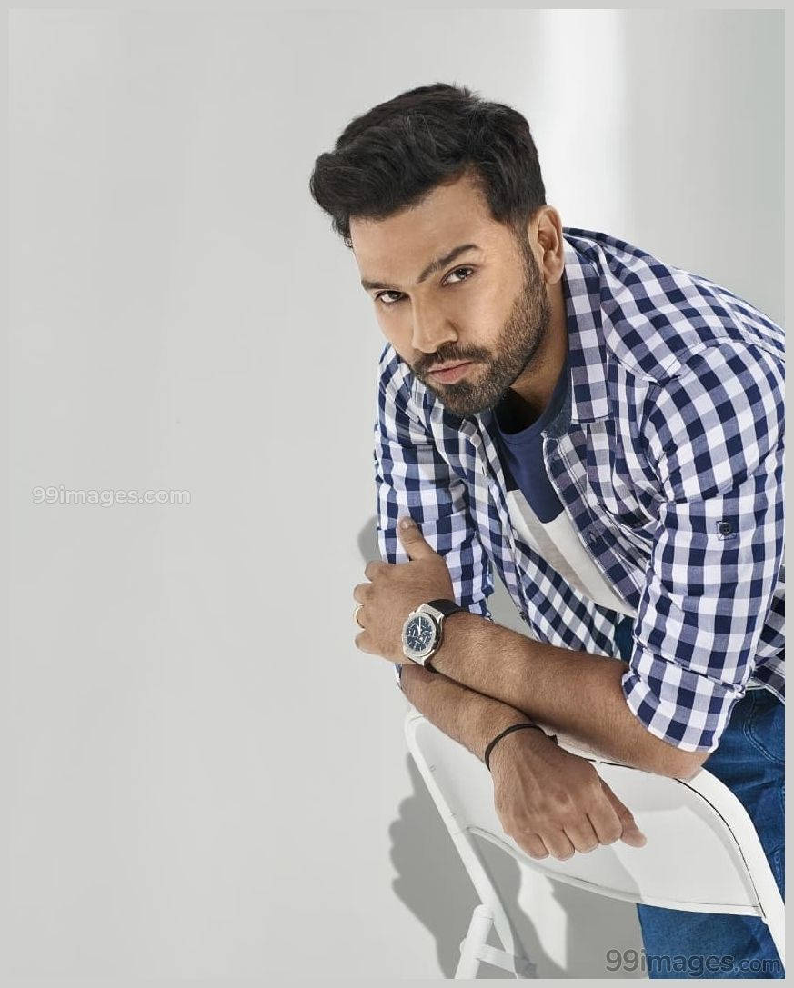 Rohit Sharma 桌布 壁紙 — 一個深色頭髮和鬍鬚的男人，穿著藍白格紋襯衫，向前傾靠在一張白色椅子上。