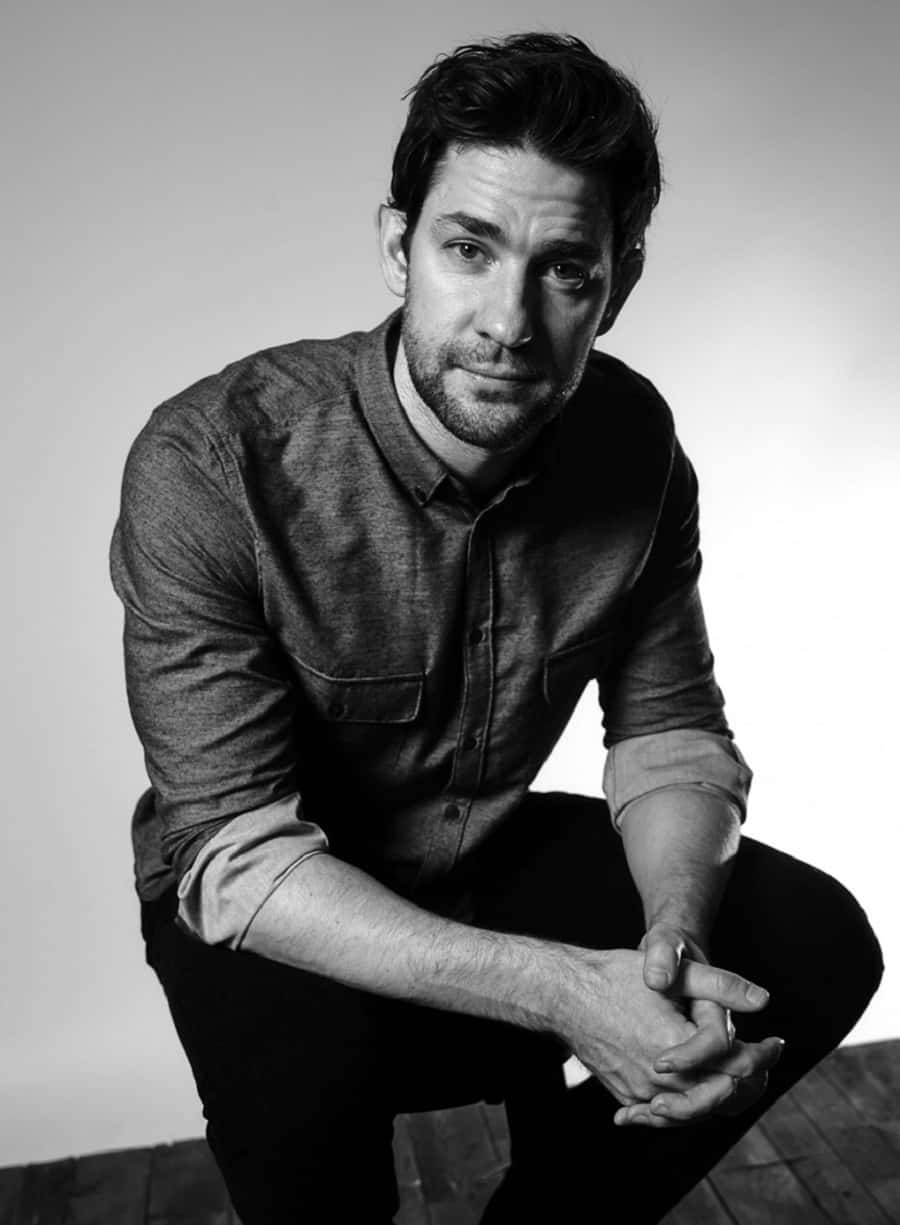 john krasinski 桌布 壁紙 — 一個深色頭髮和鬍鬚的男人在黑白工作室肖像中蹲下，雙手緊握，直視鏡頭。
