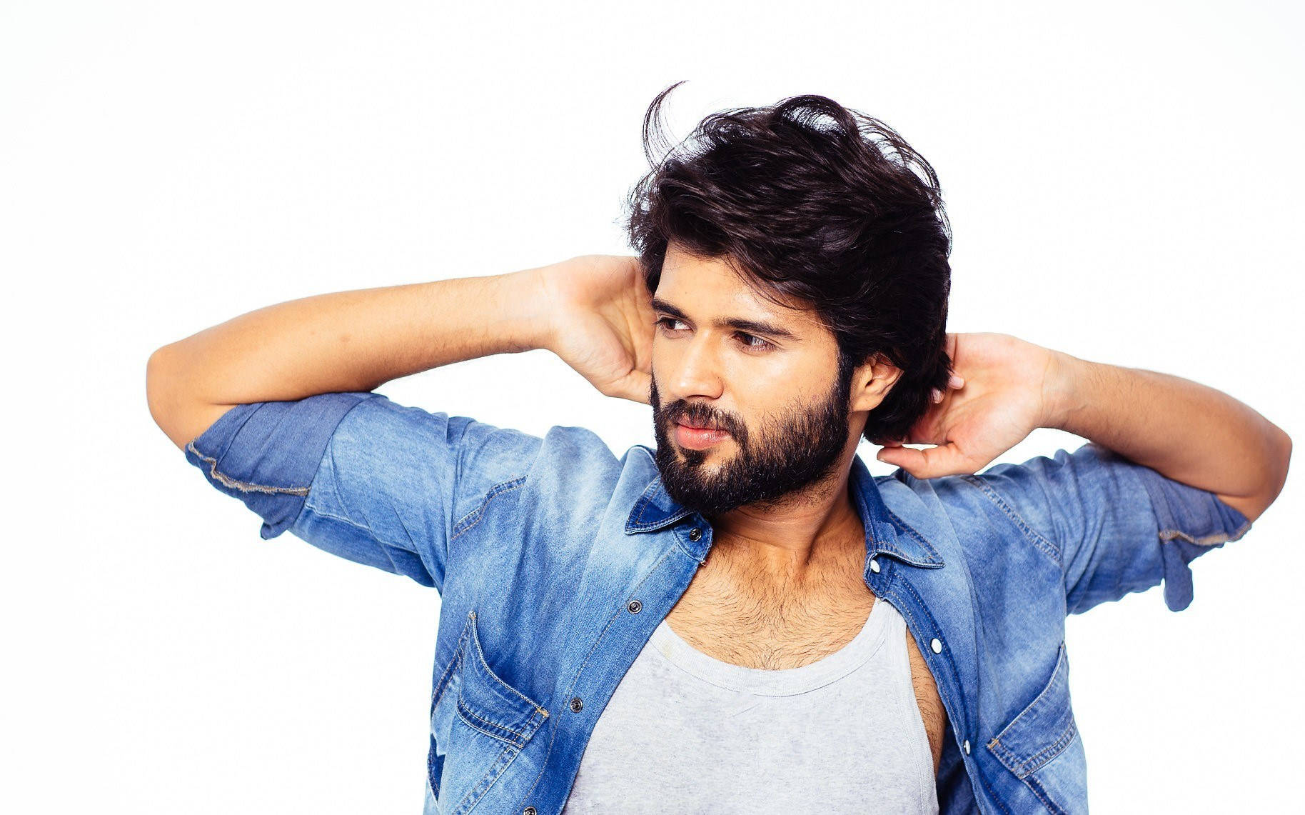 vijay devarakonda 4K 桌布 壁紙 — 一個深色頭髮和鬍鬚的男人穿著牛仔襯衫在背心外面，同時捂住耳朵以抵擋噪音。