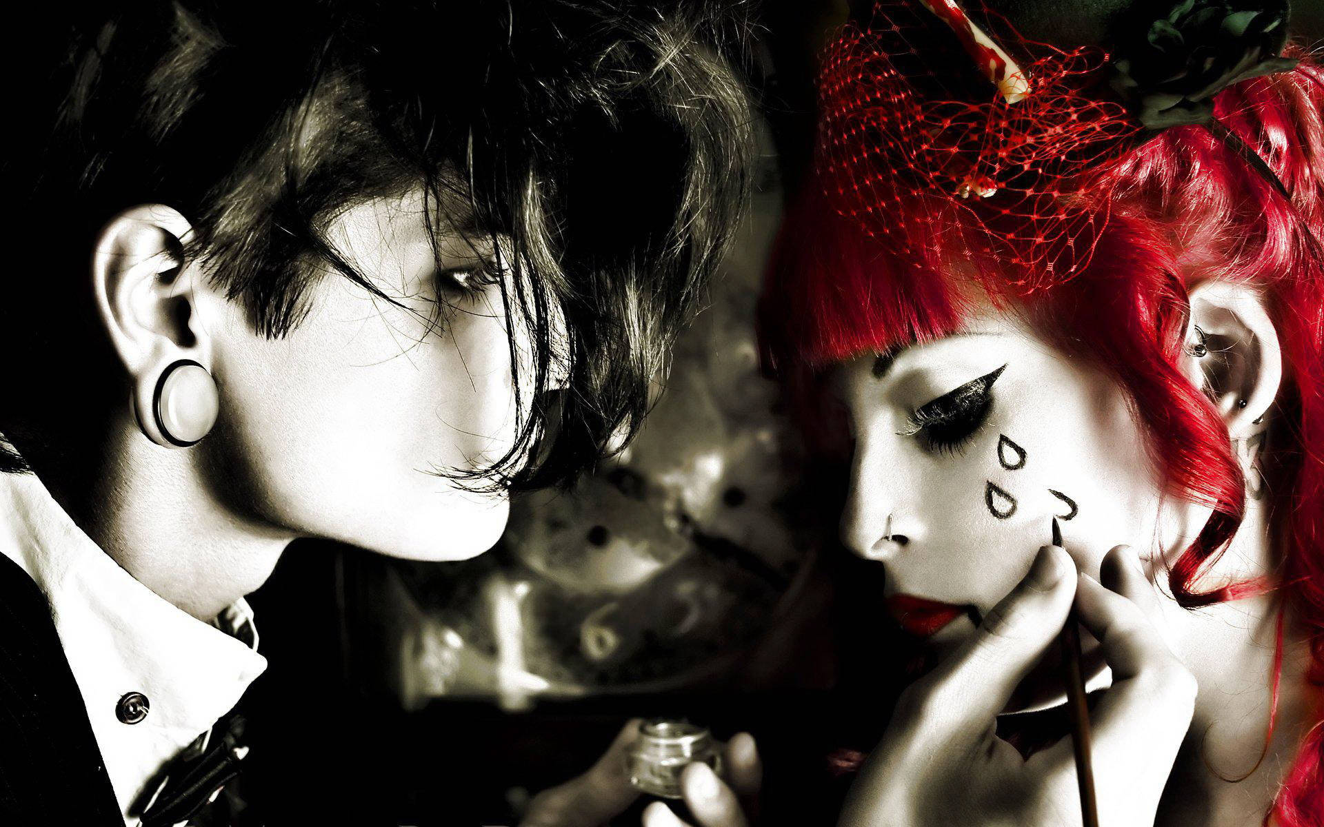 emo 桌布 壁紙 — 一個深色頭髮戴耳環的人正在為另一個擁有鮮豔紅髮和淚滴臉部彩繪的人化妝。