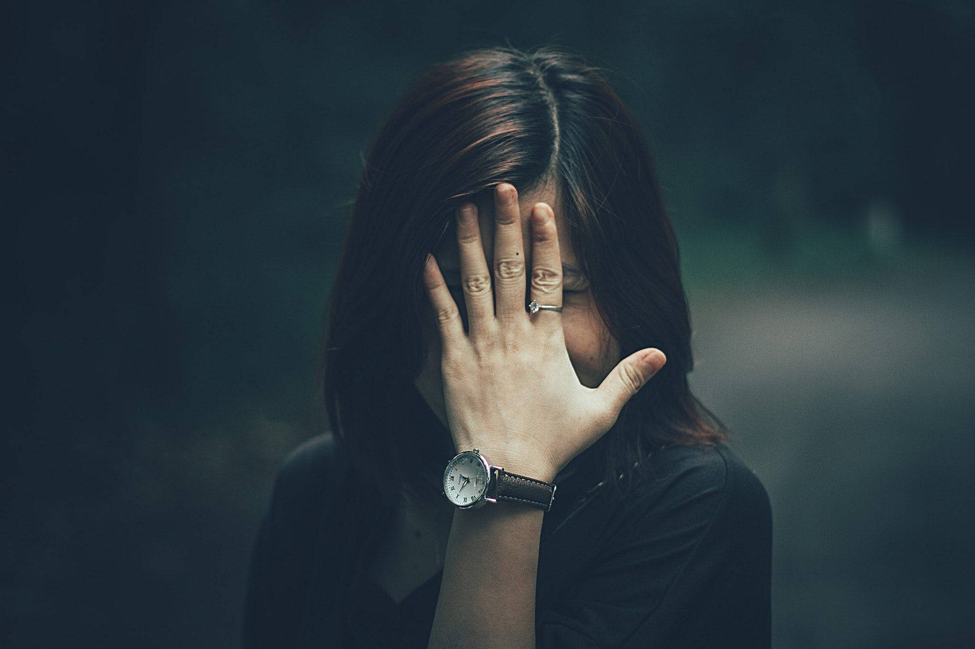 Hiding 桌布 壁紙 — 一個深色頭髮的人用一隻手遮住臉，戴著手錶和戒指，背景是模糊的暗色。