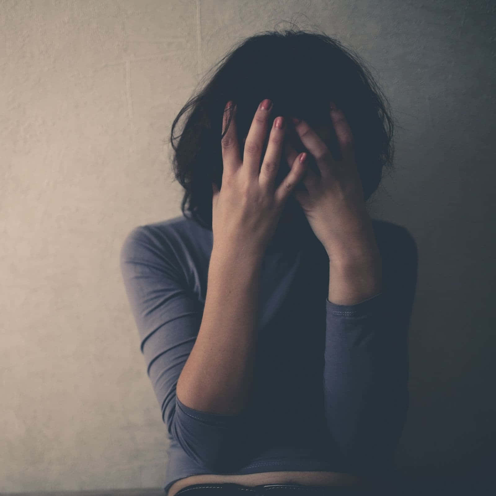 Depression Girl 桌布 壁紙 — 一個深色頭髮的人用雙手遮住臉，靠著一個普通有紋理的牆，在一個昏暗的房間裡。