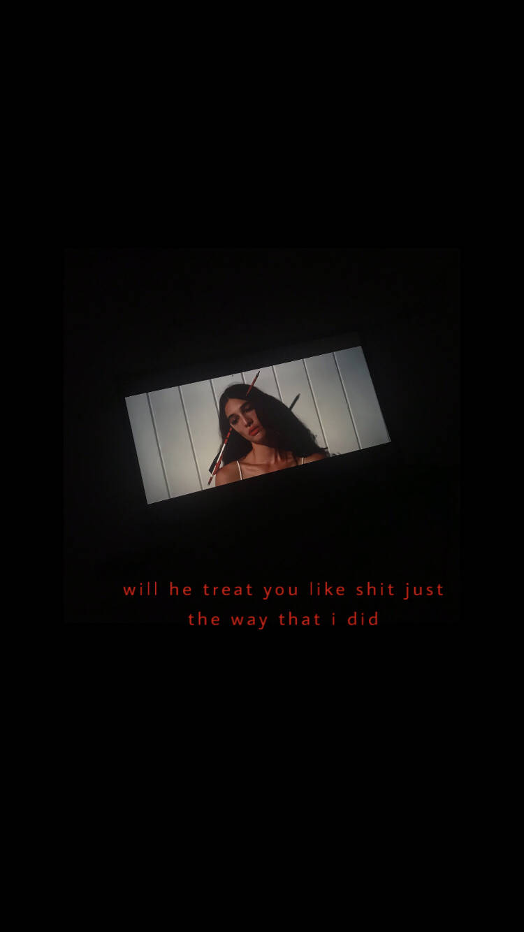 joji 桌布 壁紙 — 一個深色頭髮的女人從傾斜的螢幕上強烈地凝視，在一個黑暗的房間裡，下面有紅色文字。