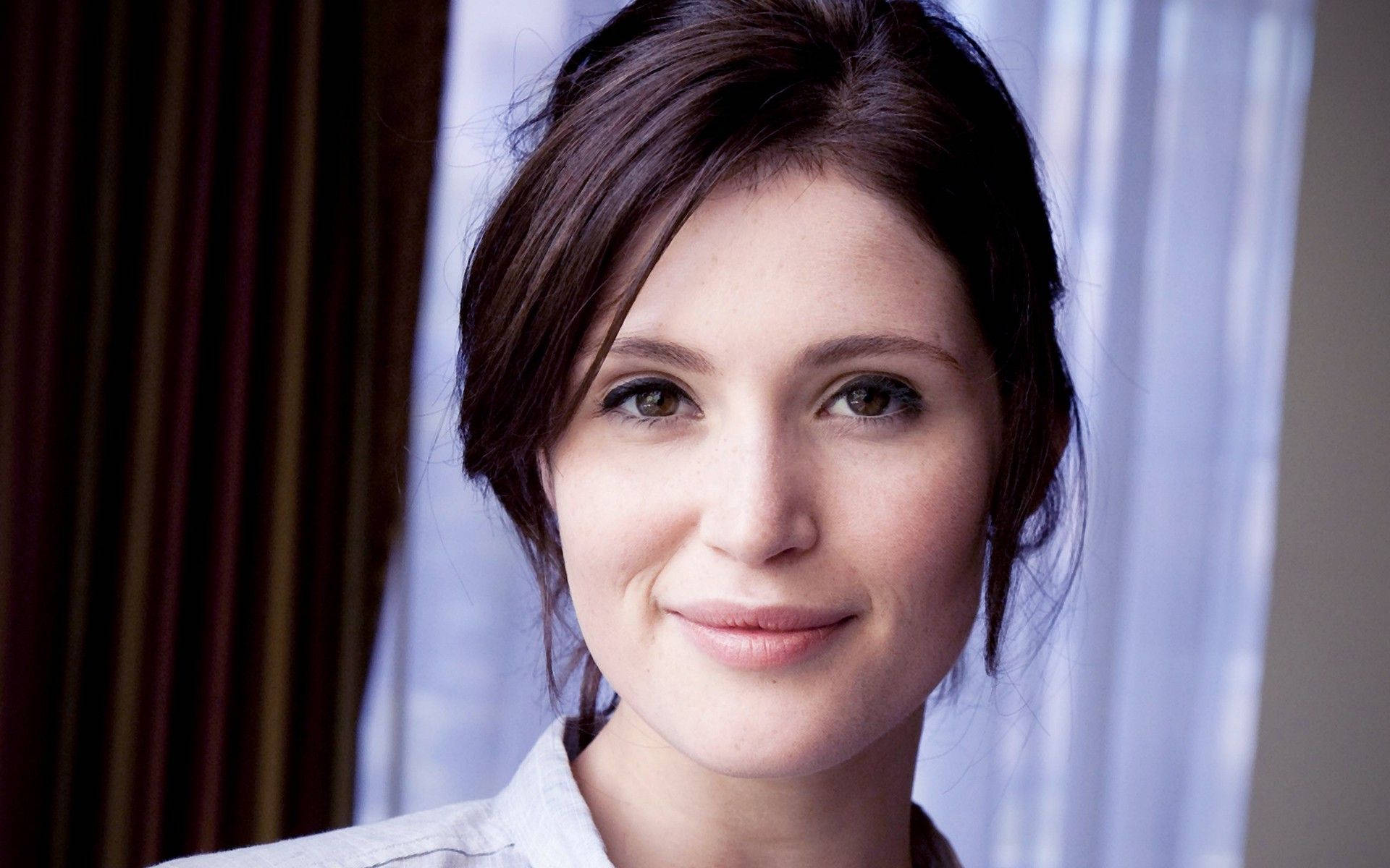 Gemma Arterton 桌布 壁紙 — 一個深色頭髮的女人的特寫肖像，在垂簾背景下溫柔微笑。