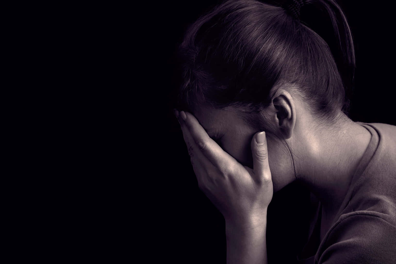 Depressing Profile 桌布 壁紙 — 一個深色頭髮紮成馬尾的人用一隻手遮住臉，背景是純黑色。