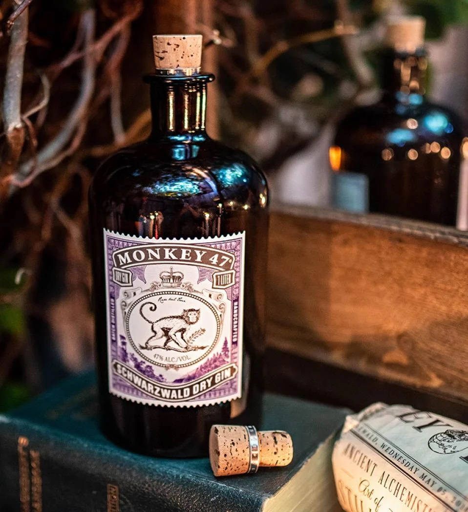 Drink 桌布 壁紙 — 一個深藍色的Monkey 47琴酒瓶連軟木塞放在復古書籍上，旁邊有另一個瓶子和一本名為Ancient Alchemist的書。
