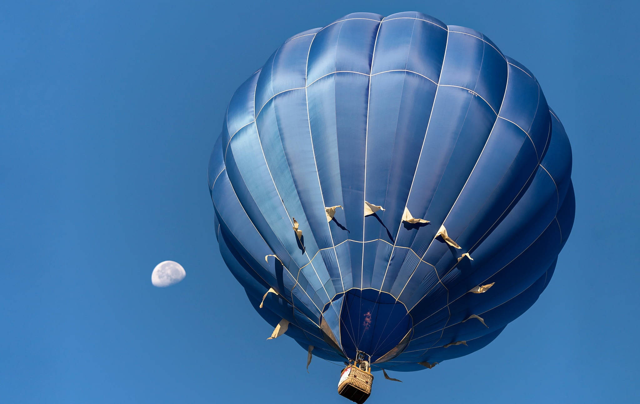 Hot Air Balloon 桌布 壁紙 — 一個深藍色的熱氣球在晴朗的天空中漂浮，附近有一彎新月。