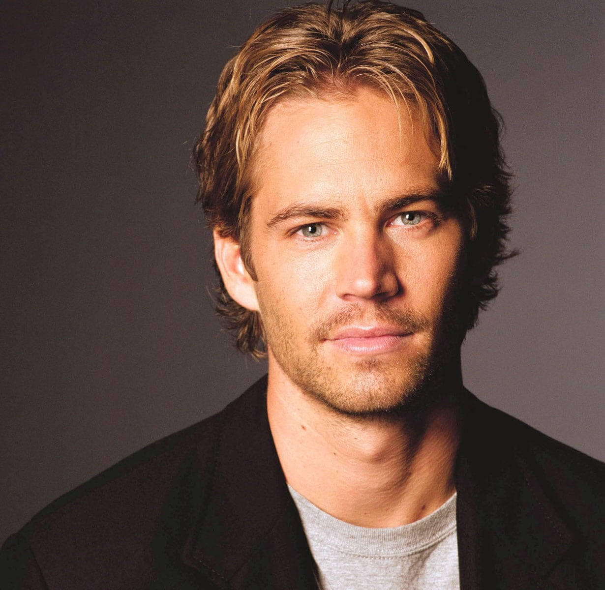 Paul Walker 桌布 壁紙 — 一個淺棕色頭髮、綠色眼睛的男人，身穿黑色外套配灰色T恤，背景為深灰色的特寫肖像。