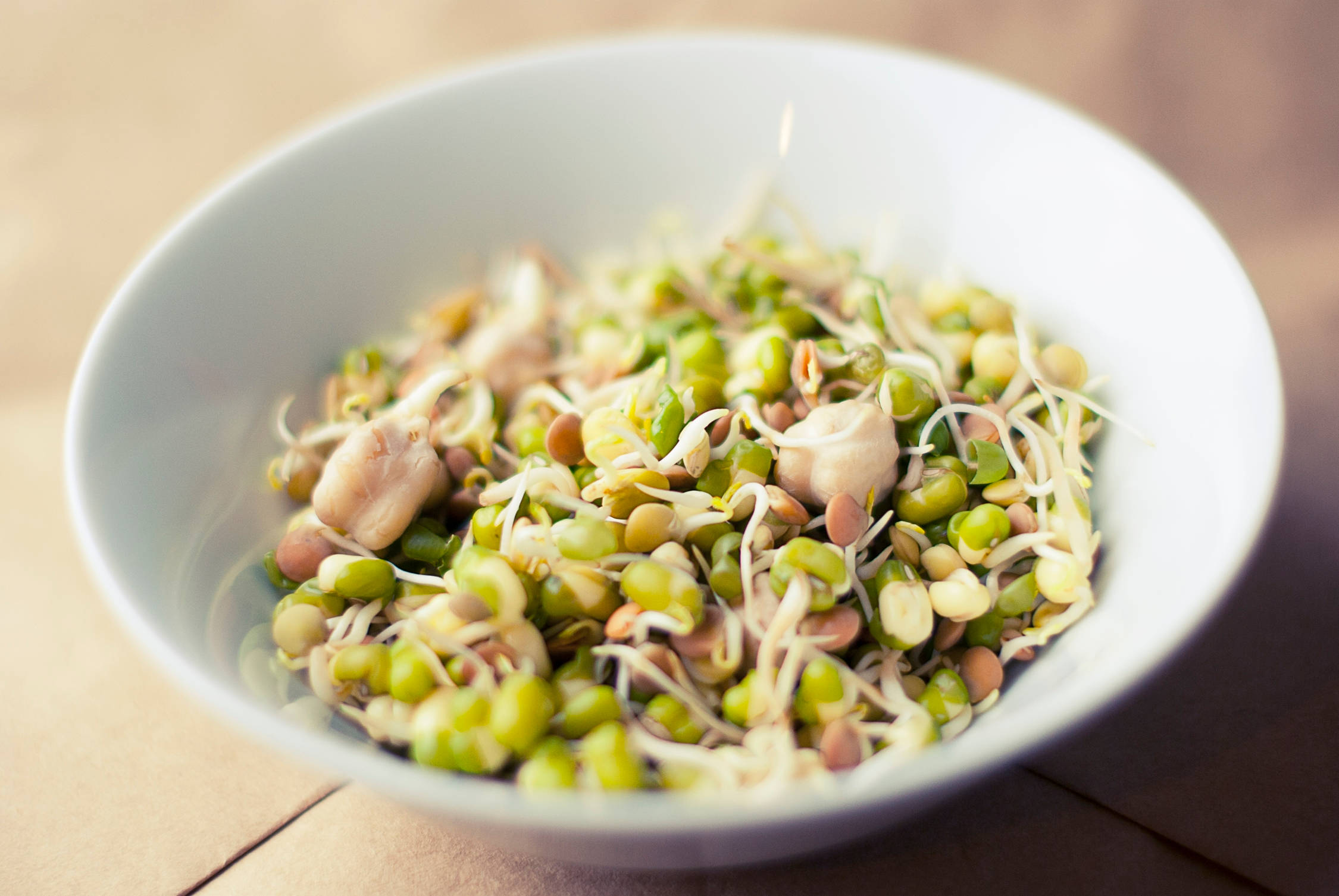 beans 桌布 壁紙 — 一個淺白色碗，盛滿新鮮綠色芽菜和豆類，放在溫暖的木質表面上。