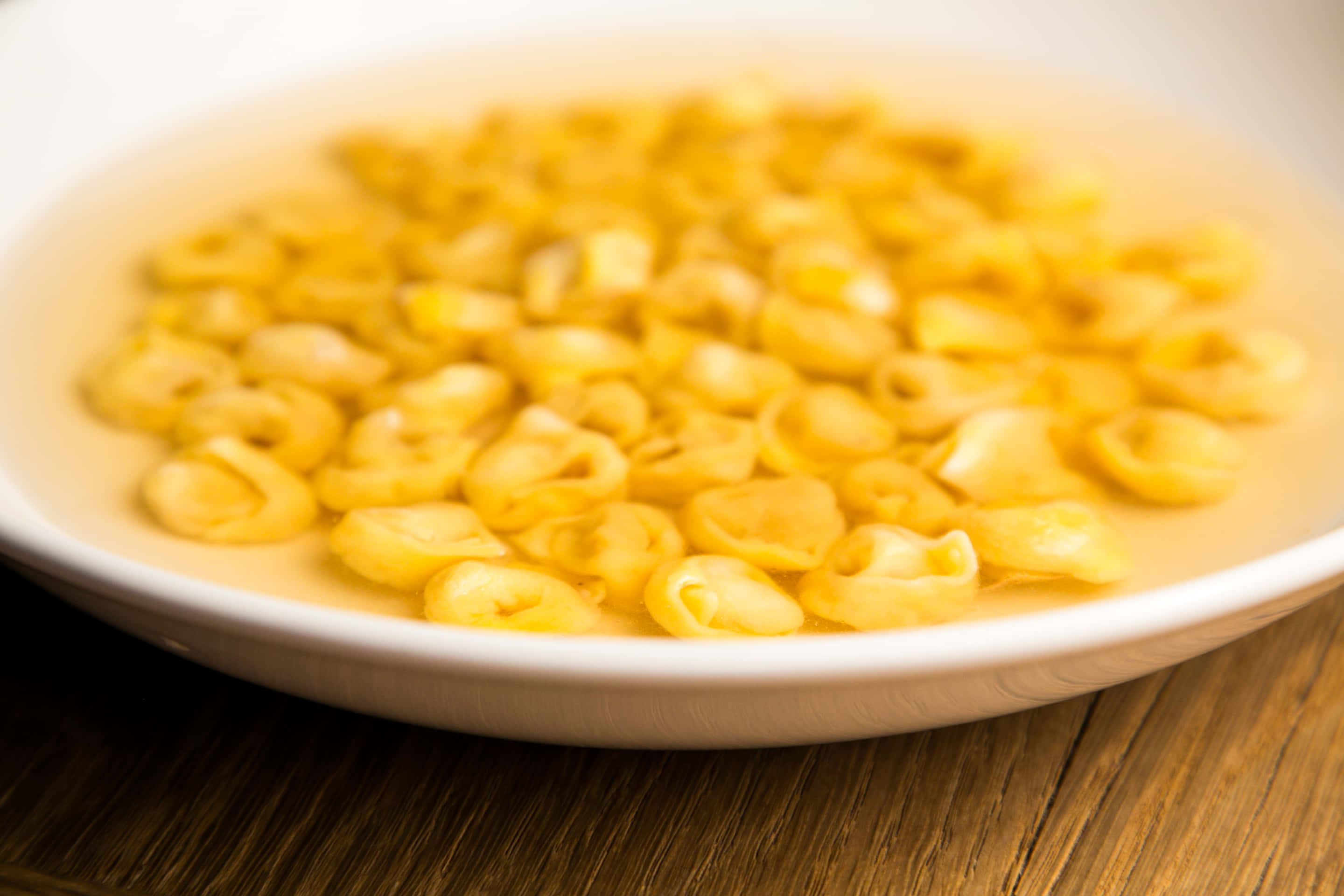 Pasta 桌布 壁紙 — 一個淺白色碗盛載著淡黃色義大利雲吞漂浮在熱湯中，放在木桌上。