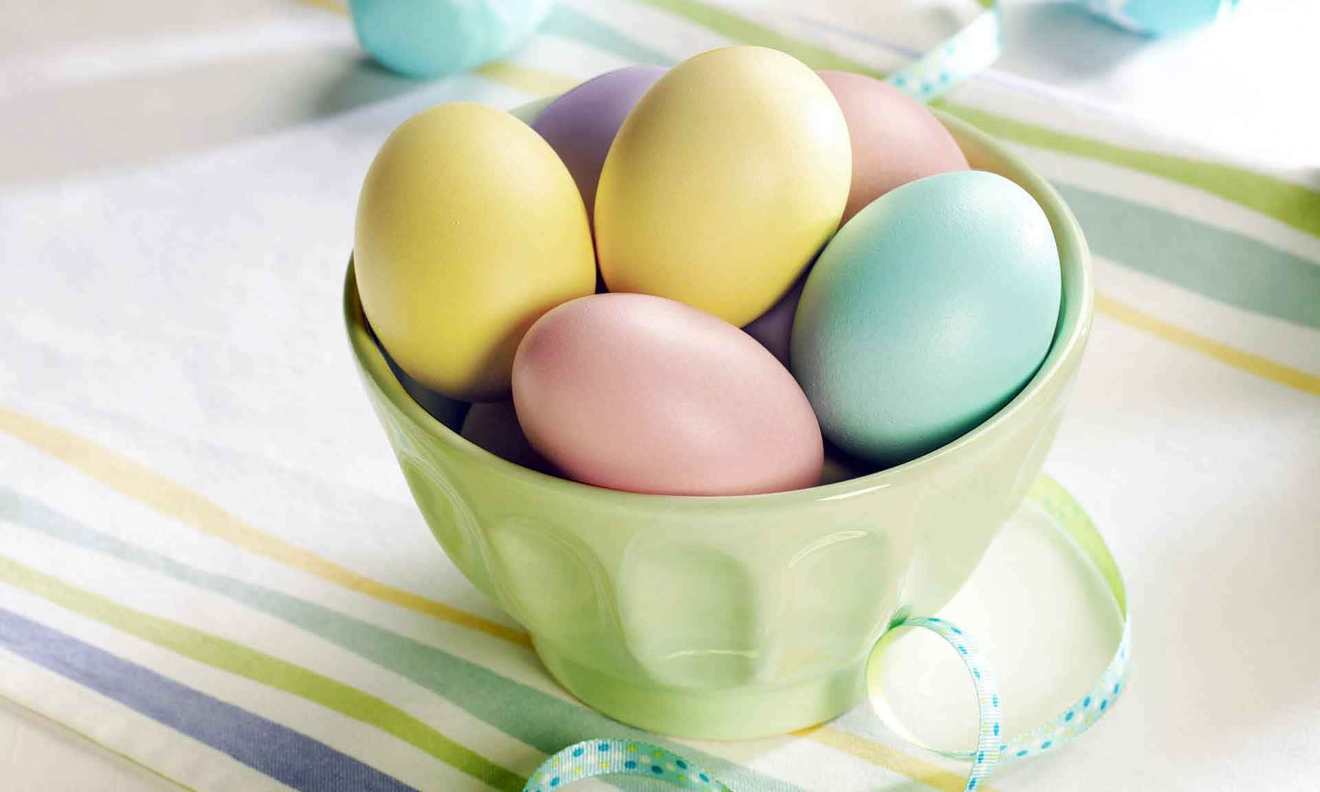 Pastel Easter 桌布 壁紙 — 一個淺綠色碗盛裝著放在條紋布上的粉彩復活節彩蛋，旁邊有一條絲帶。