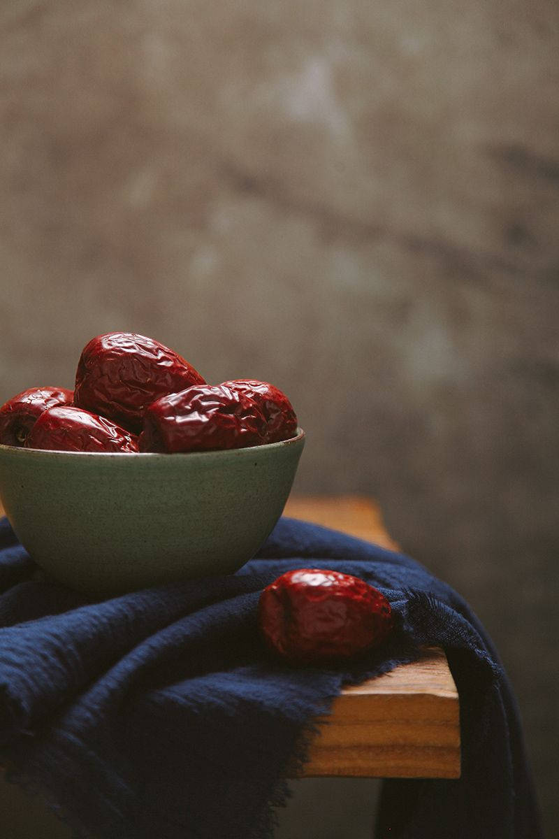 bowl 桌布 壁紙 — 一個淺綠色碗盛載著飽滿的紅色棗子，放在覆蓋木質表面的深藍色布上。