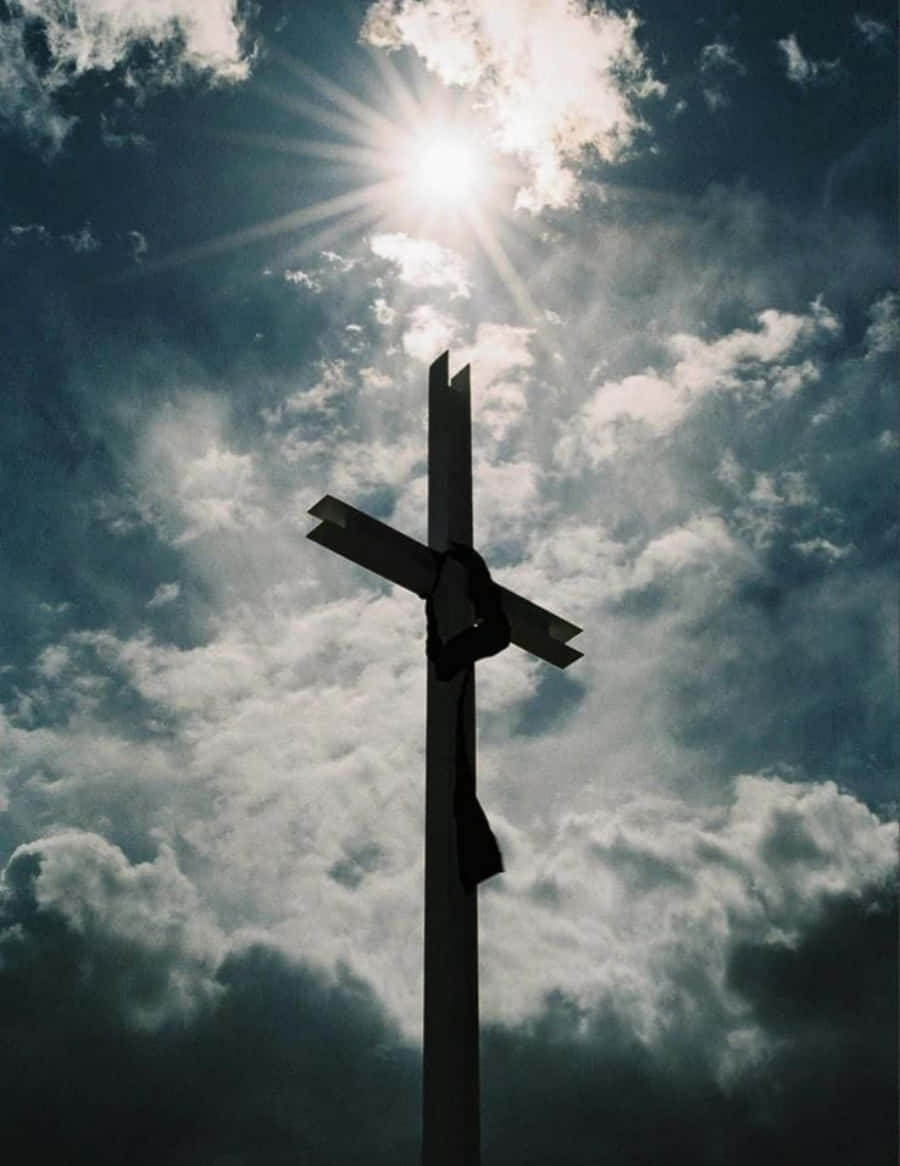 Beautiful Cross 桌布 壁紙 — 一個清晰的十字架剪影，在戲劇性的天空下，陽光穿透烏雲形成光芒四射的景象。