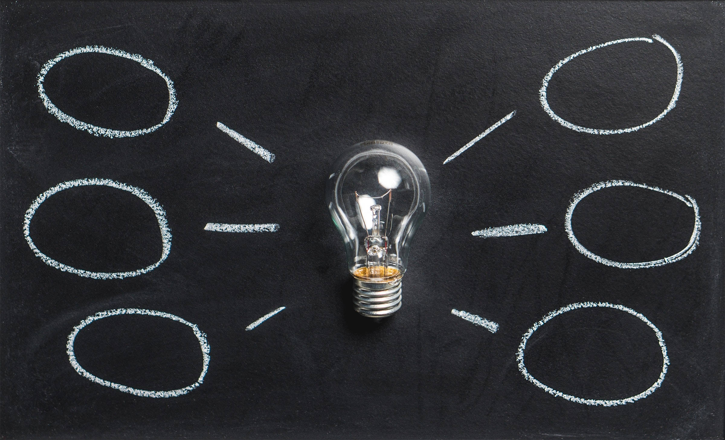 Light Bulb 桌布 壁紙 — 一個清晰的燈泡位於黑色黑板的中央，周圍有粉筆畫的圓圈和線條，暗示著腦力激盪或創意產生。