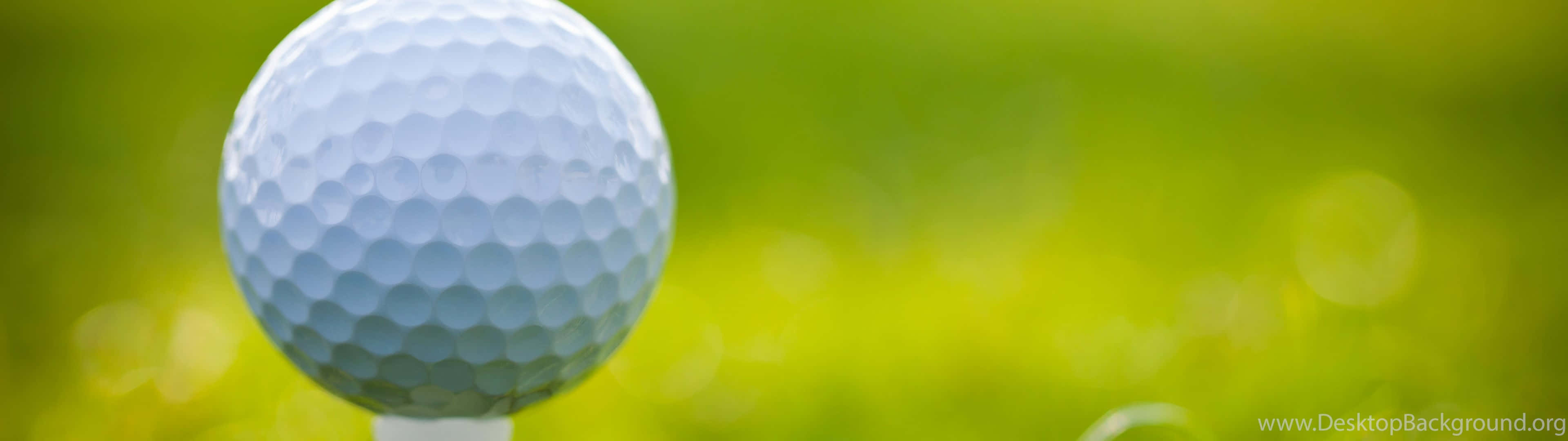 Golf 3840x1080 桌布 壁紙 — 一個清晰的白高爾夫球放在球座上，背景是充滿活力的綠色模糊草地。