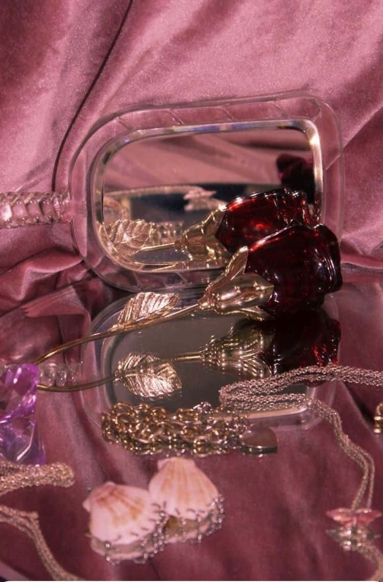 Boujee 桌布 壁紙 — 一個清晰的粉盒鏡的特寫，反射出一朵紅玫瑰和金色珠寶在華麗的紫色天鵝絨布料上。