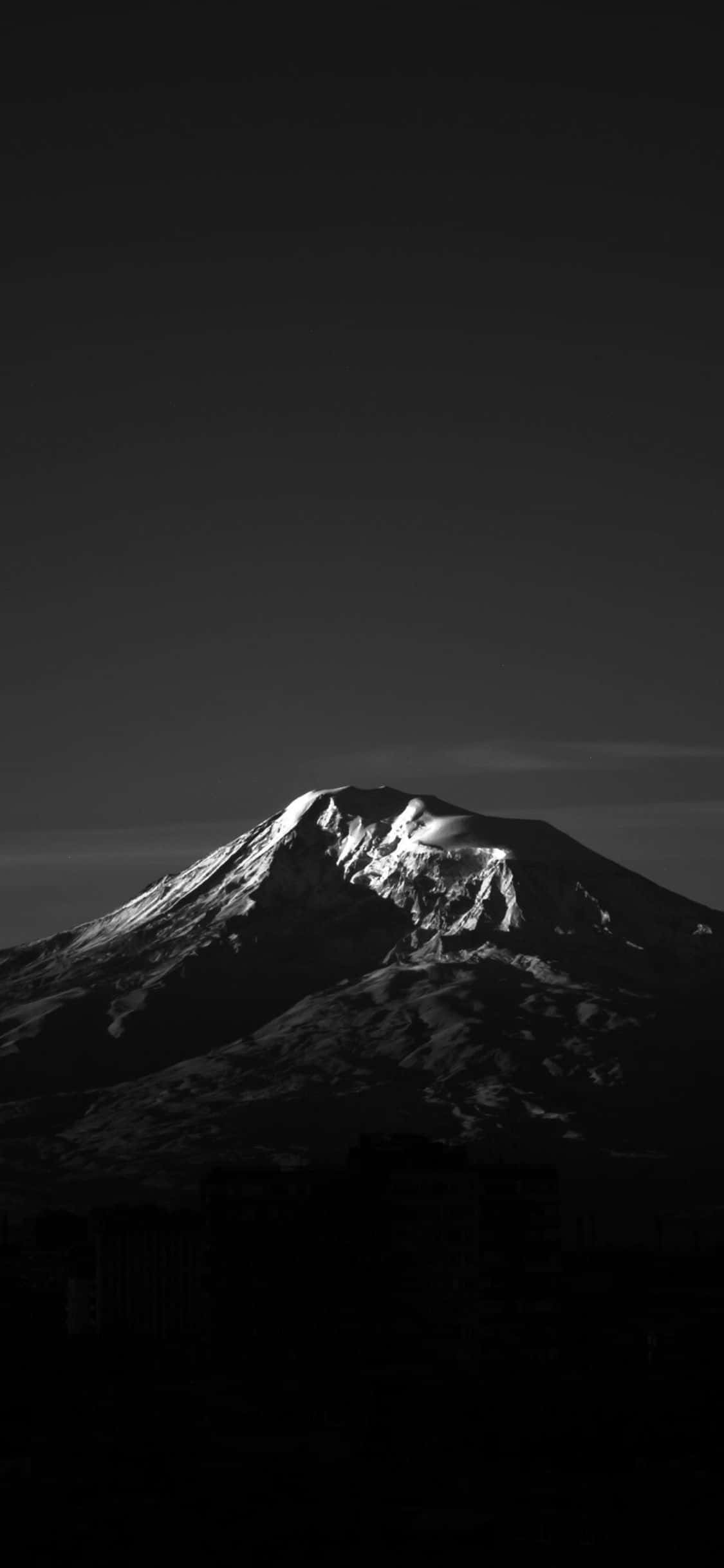 深色 iPhone 桌布 壁紙 — 一個清晰的黑白山頂，積雪的山頂在黑暗的天空下，在剪影般的城市建築上方發光。