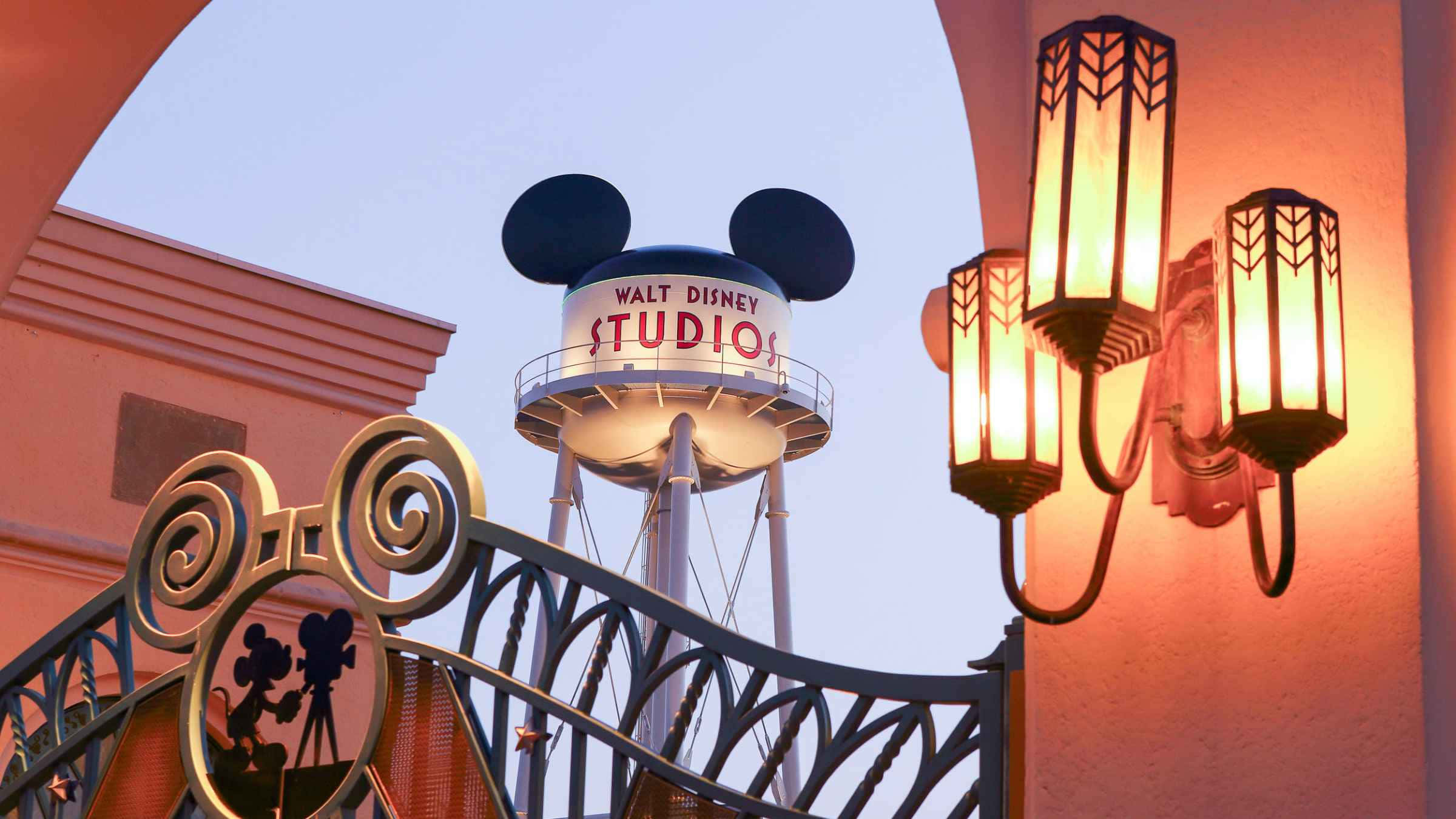 Walt Disney Studios Motion 桌布 壁紙 — 一個溫暖照亮的拱門框住了一個米奇老鼠剪影大門和一個帶有米奇耳朵的水塔，背景是黃昏的天空。